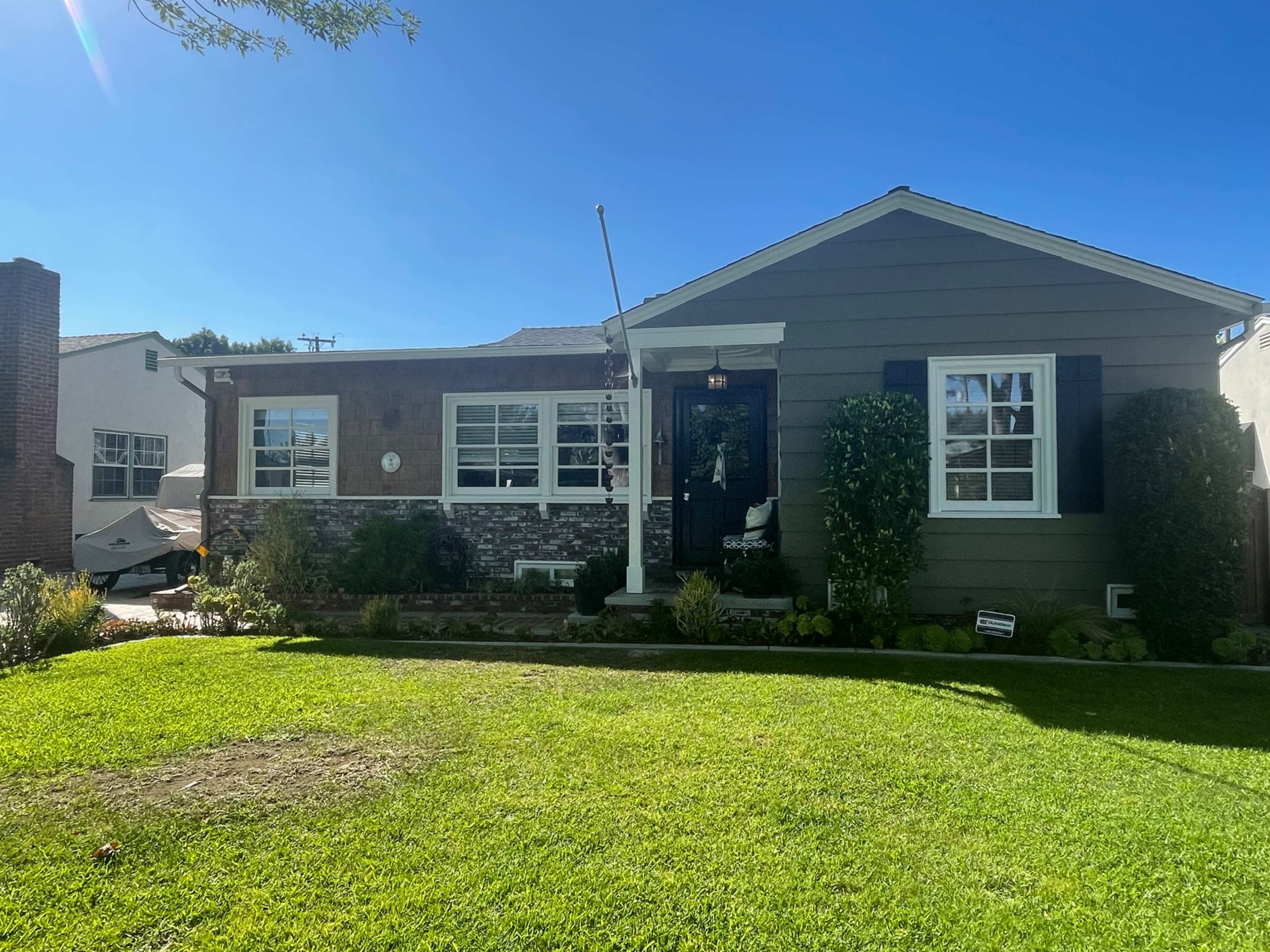A single-story house with a brick façade and green siding, surrounded by a well-maintained lawn and garden.