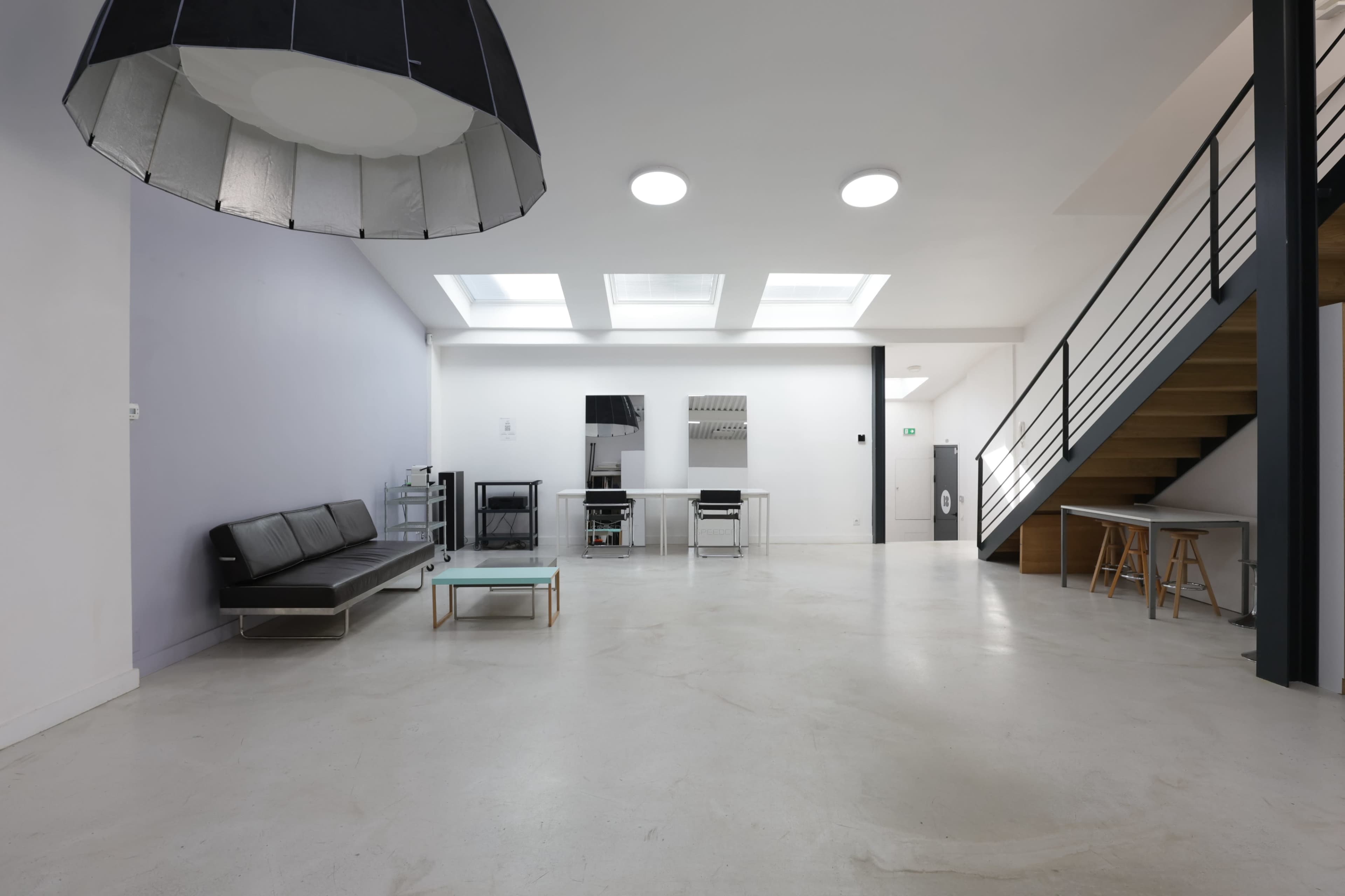 The image shows an open, modern interior space featuring a staircase, a sofa, a dining table, and large skylights.