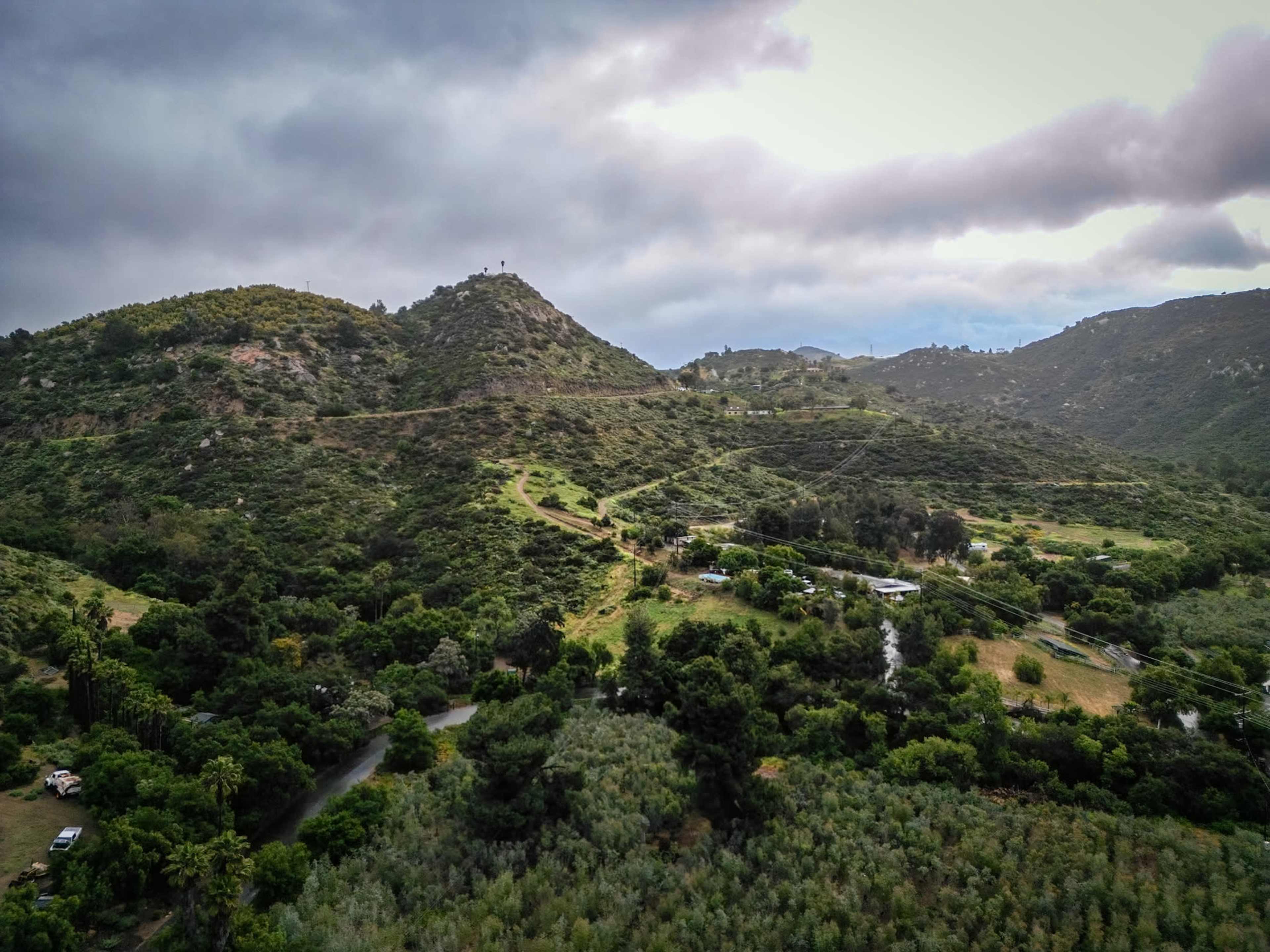 The image shows a hilly landscape covered in dense greenery under a cloudy sky.