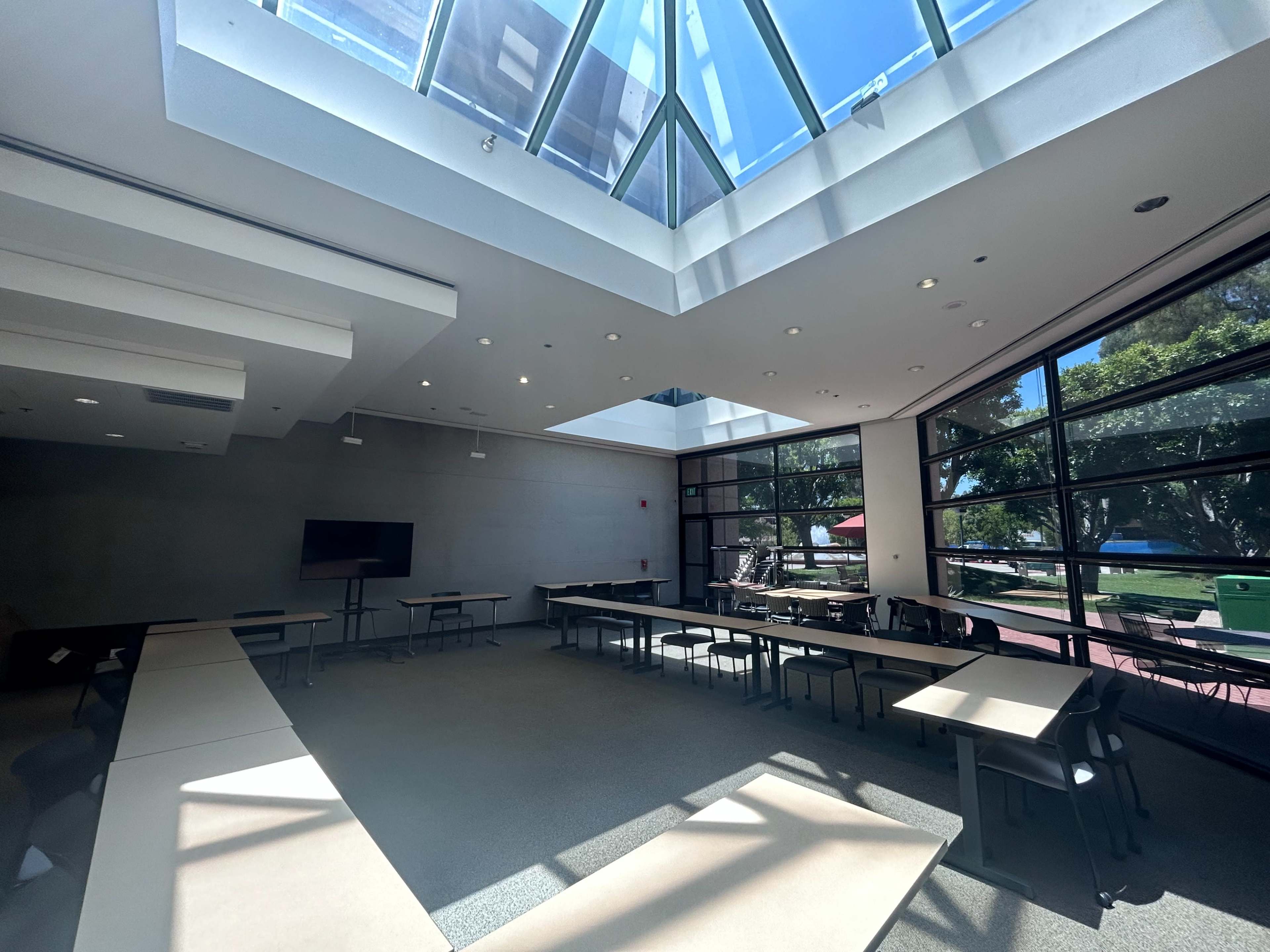 A spacious conference room with large windows, a skylight, and several tables arranged for meetings.