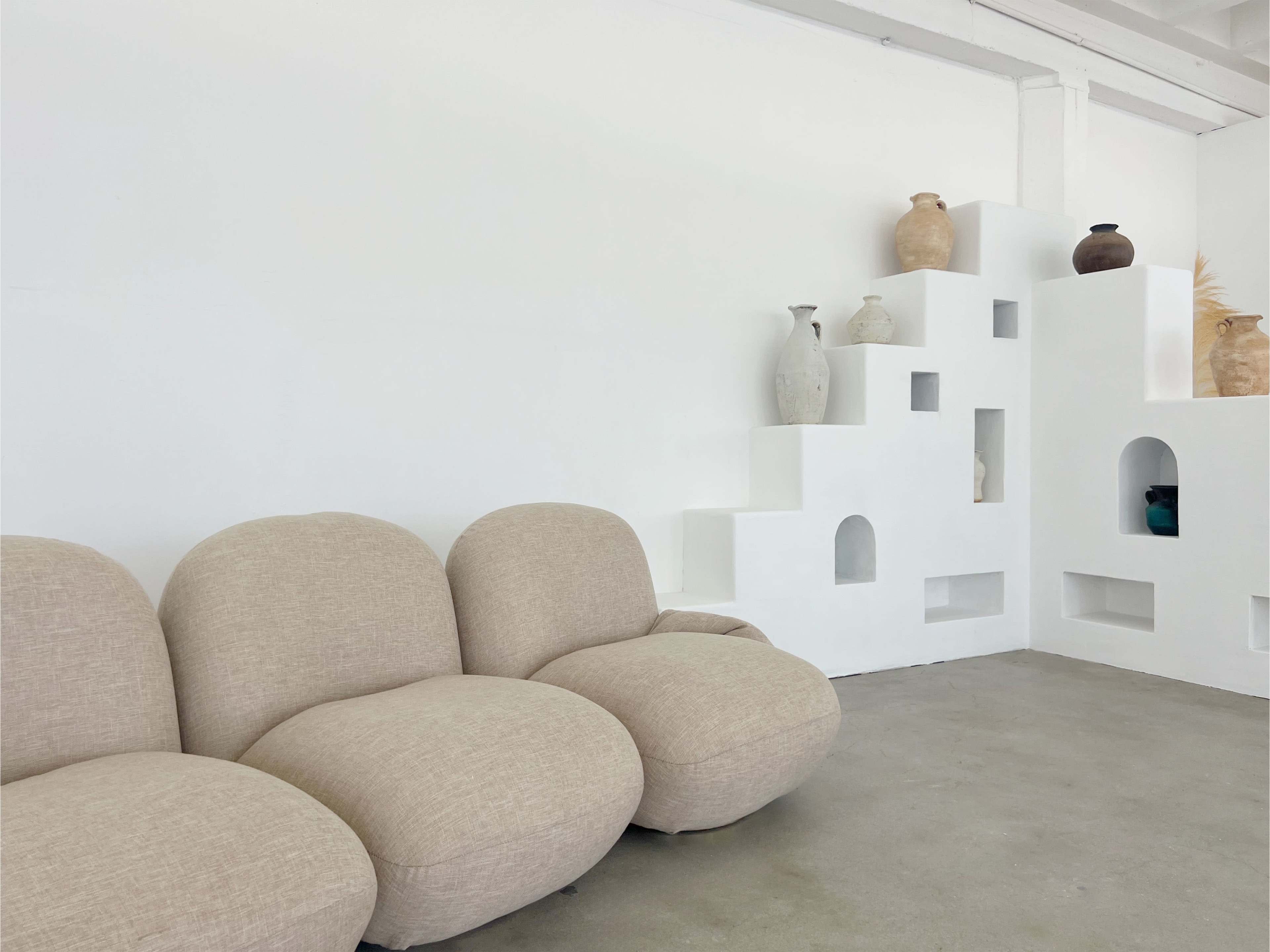 A light-colored, contemporary sofa is positioned in front of a white wall featuring decorative niches filled with various vases.