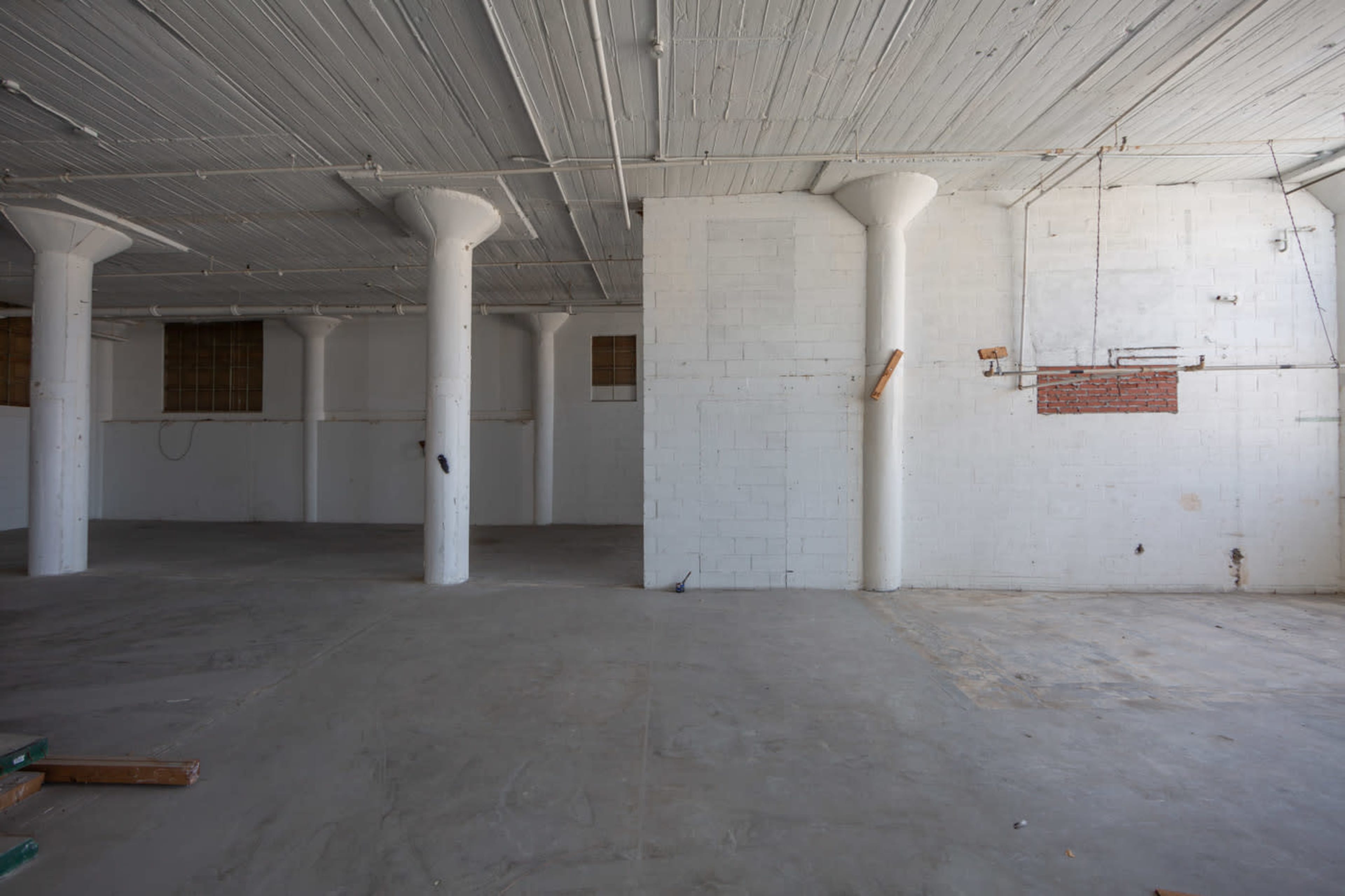 A spacious, empty room with concrete floors and several white support columns.