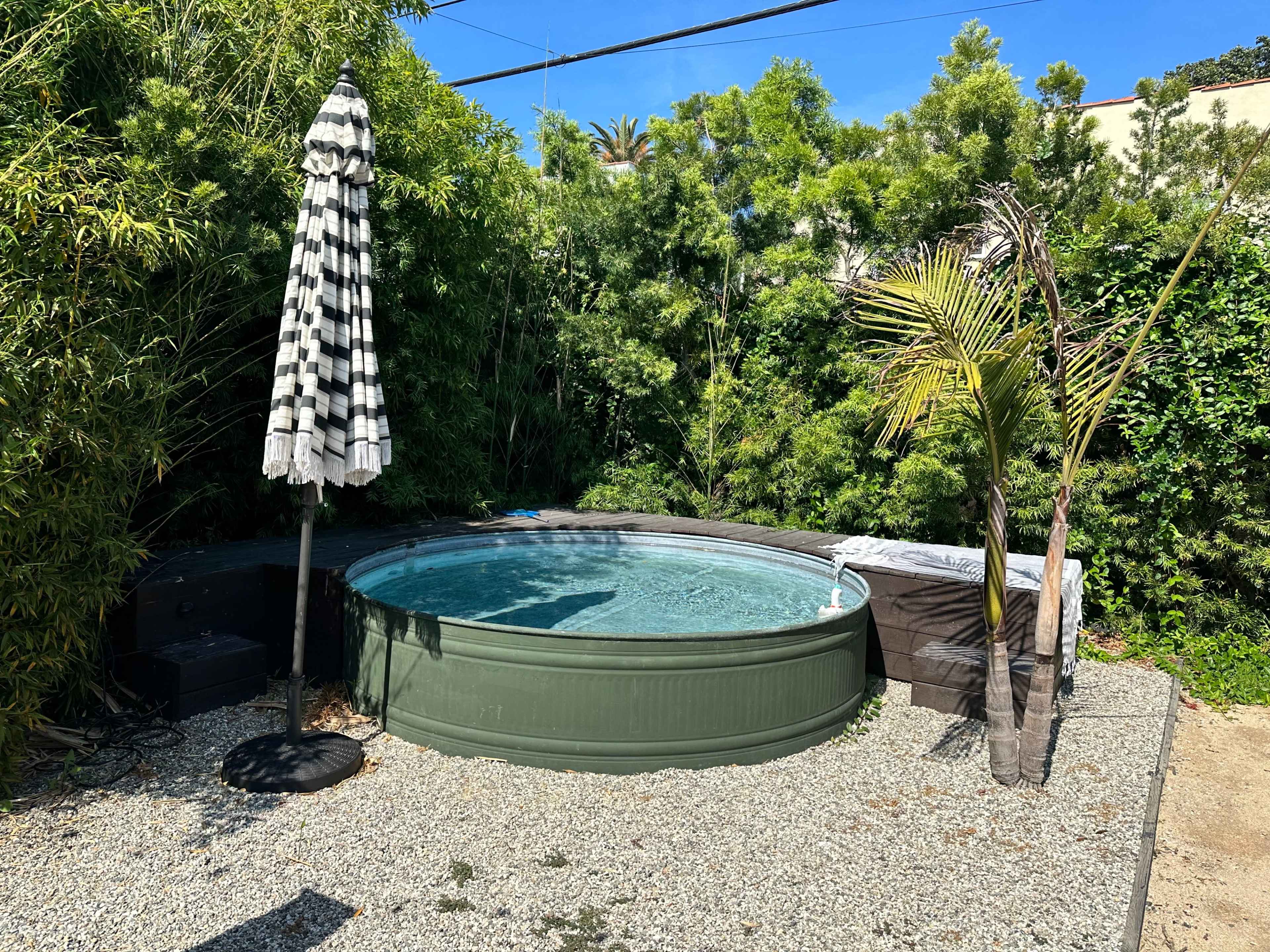 The image shows a circular above-ground hot tub surrounded by greenery and a striped outdoor umbrella.