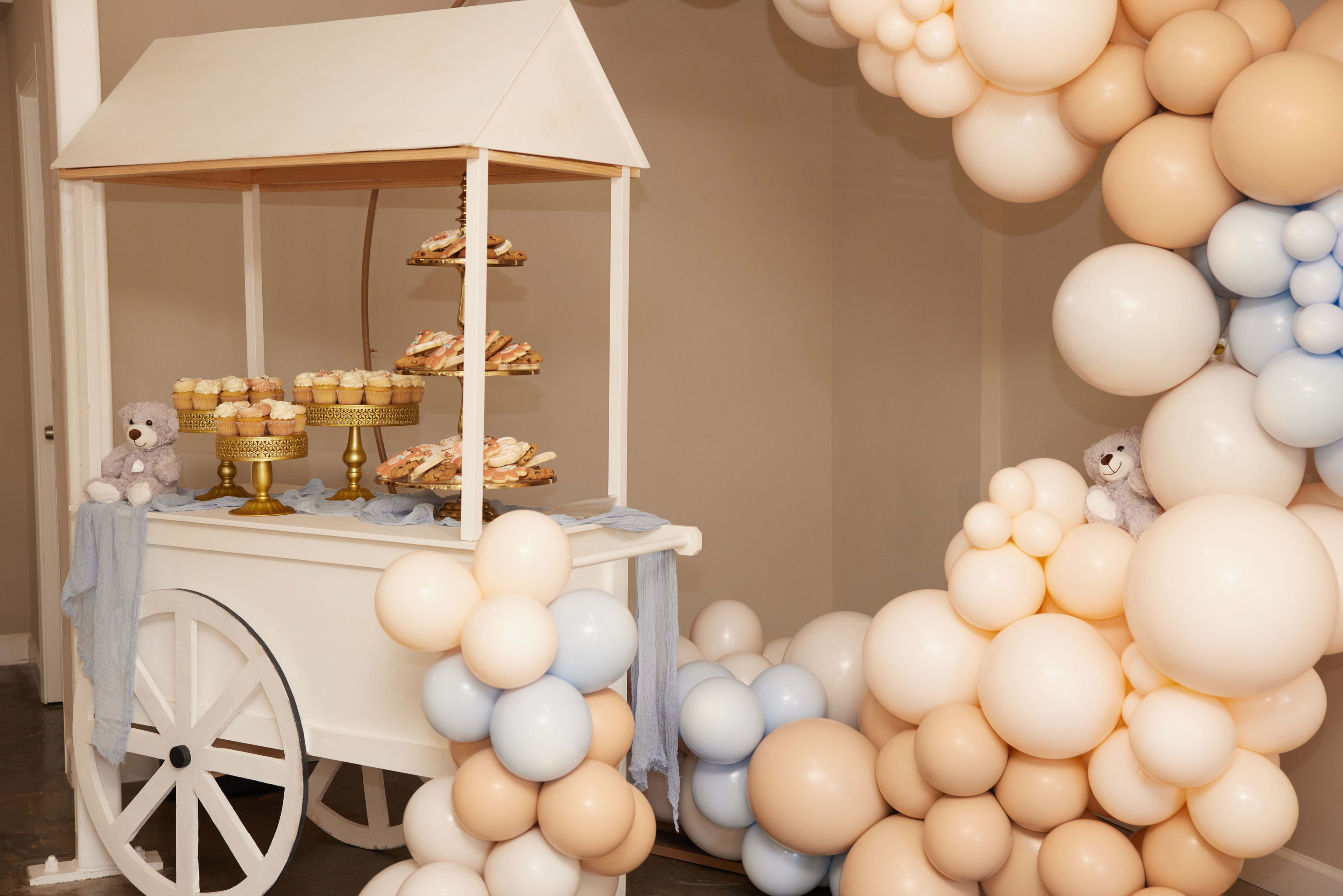 Un carrito blanco con un montón de globos para un baby shower con ositos de peluche.