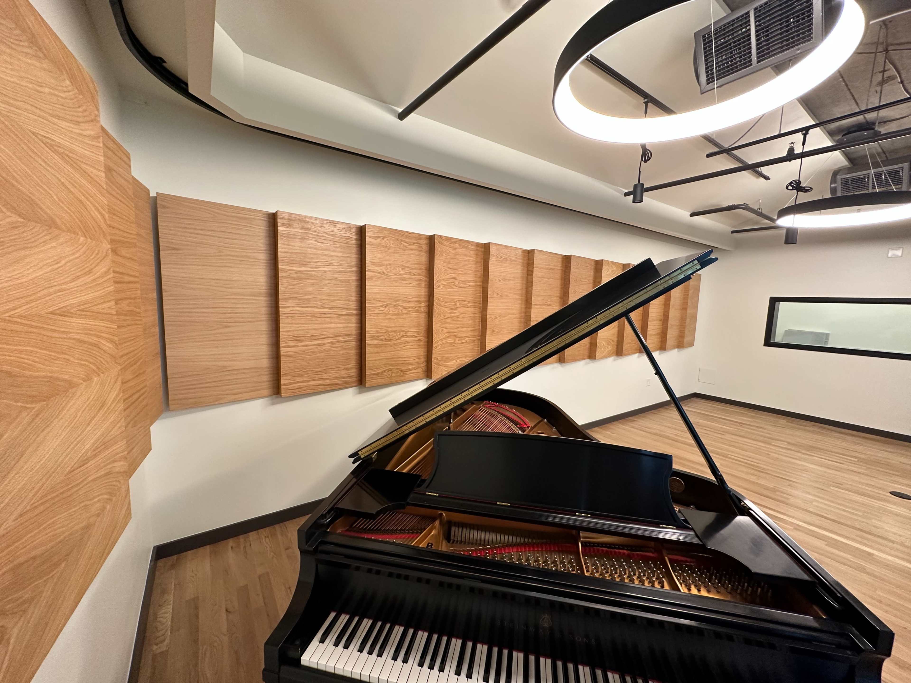 A grand piano is positioned in a soundproof room with wooden acoustic panels lining the walls.