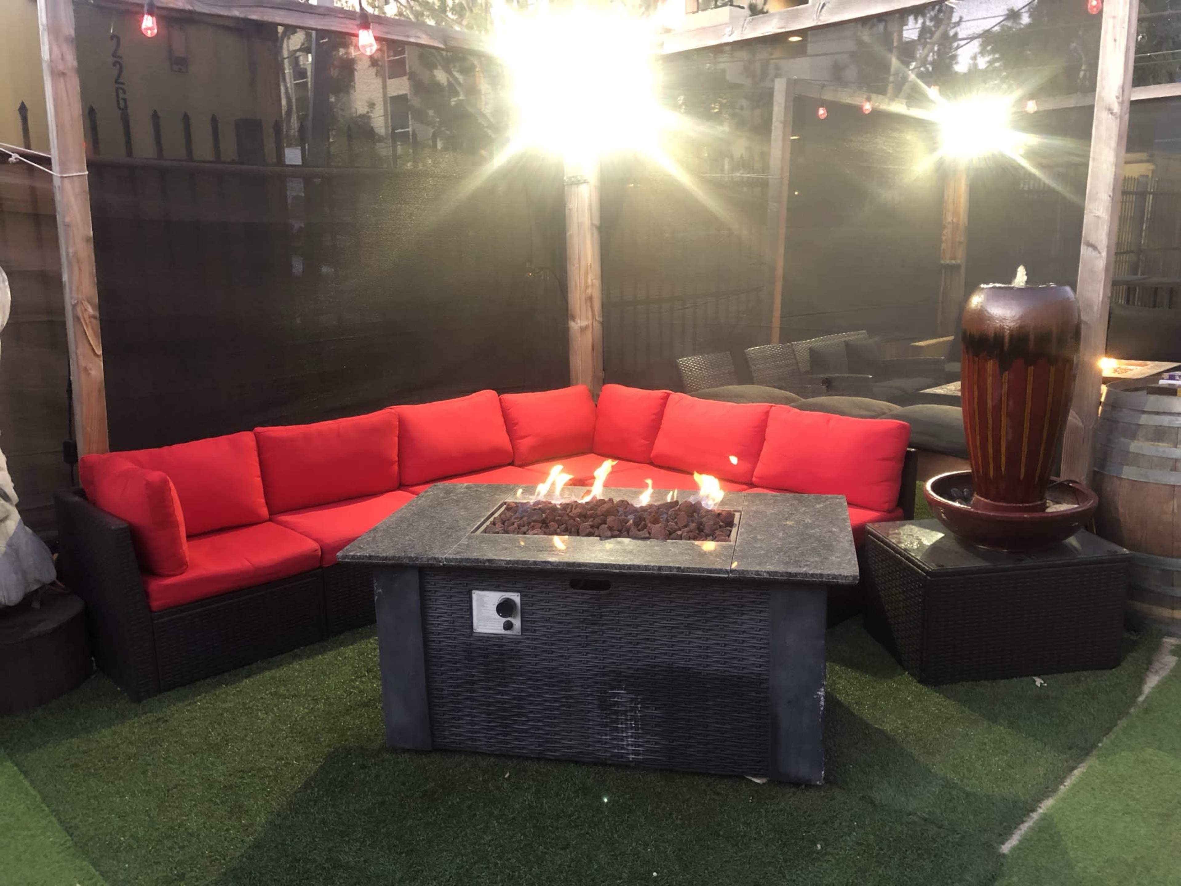 The outdoor area features a red cushioned sectional sofa surrounding a stone fire table, with a fountain and ambient lighting in the background.