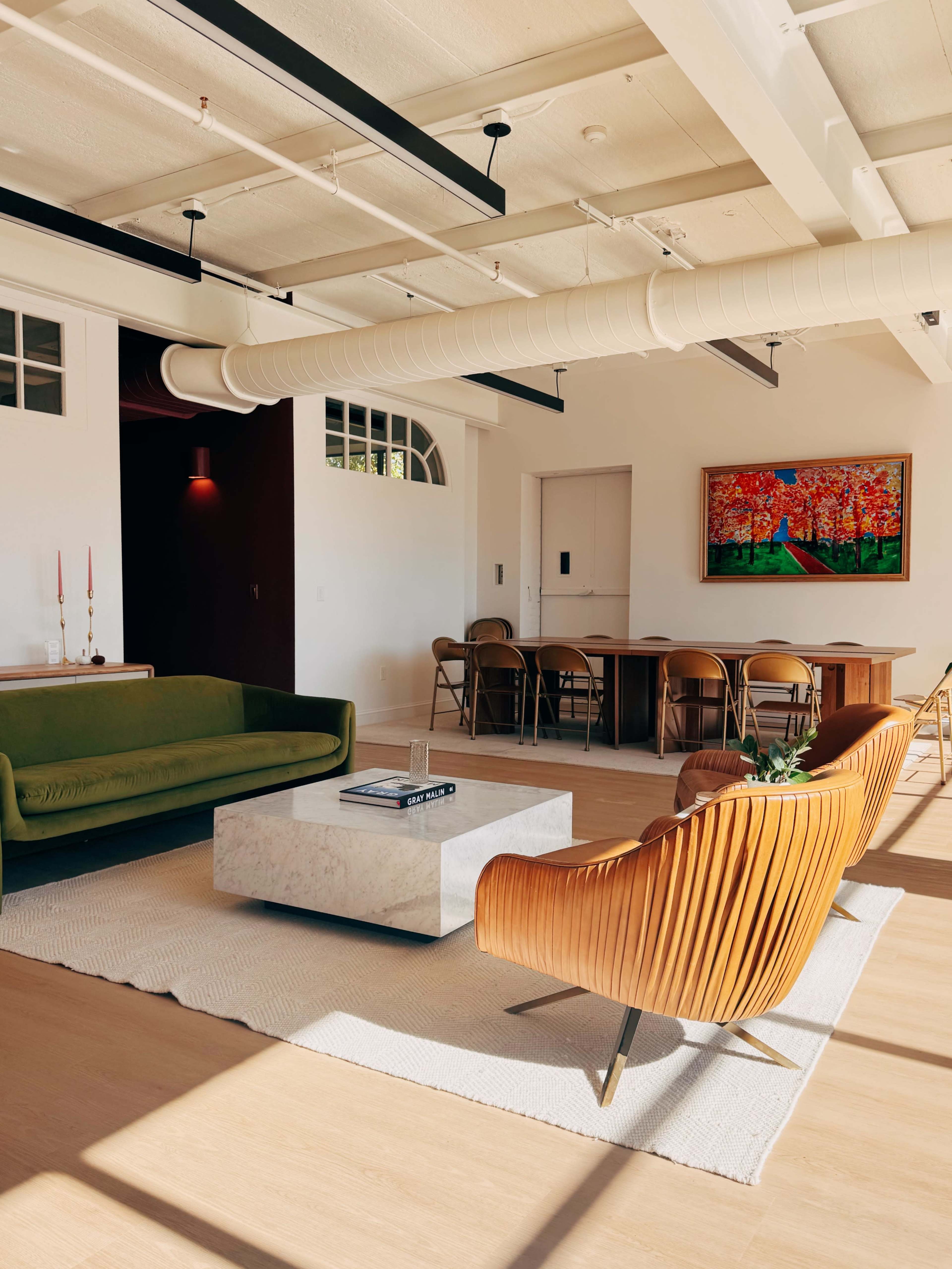 The image features a modern living space with a green sofa, orange armchairs, a marble coffee table, and a dining area with wooden chairs.