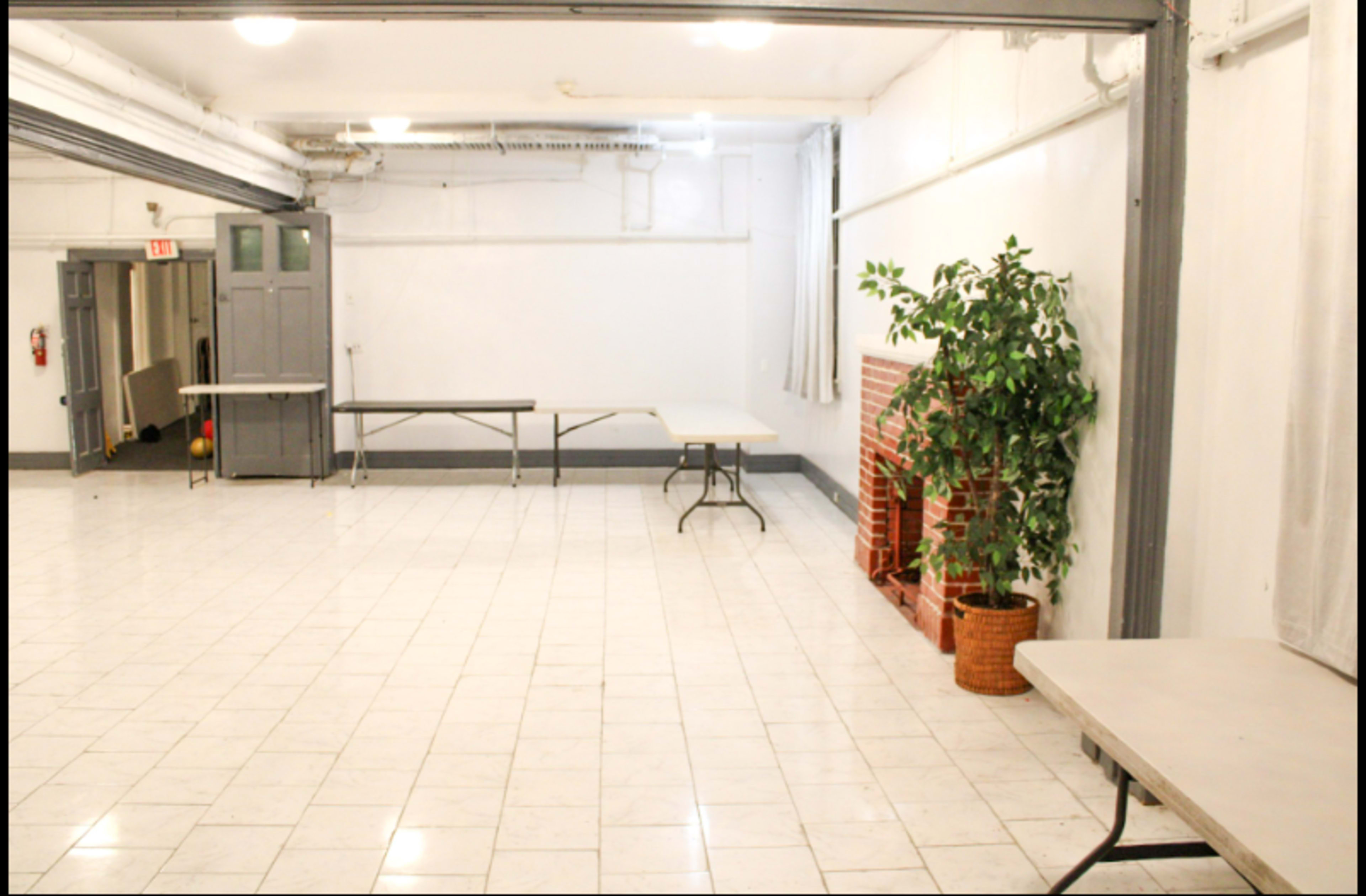 A spacious indoor area features several folding tables, a potted plant, and tiled flooring.