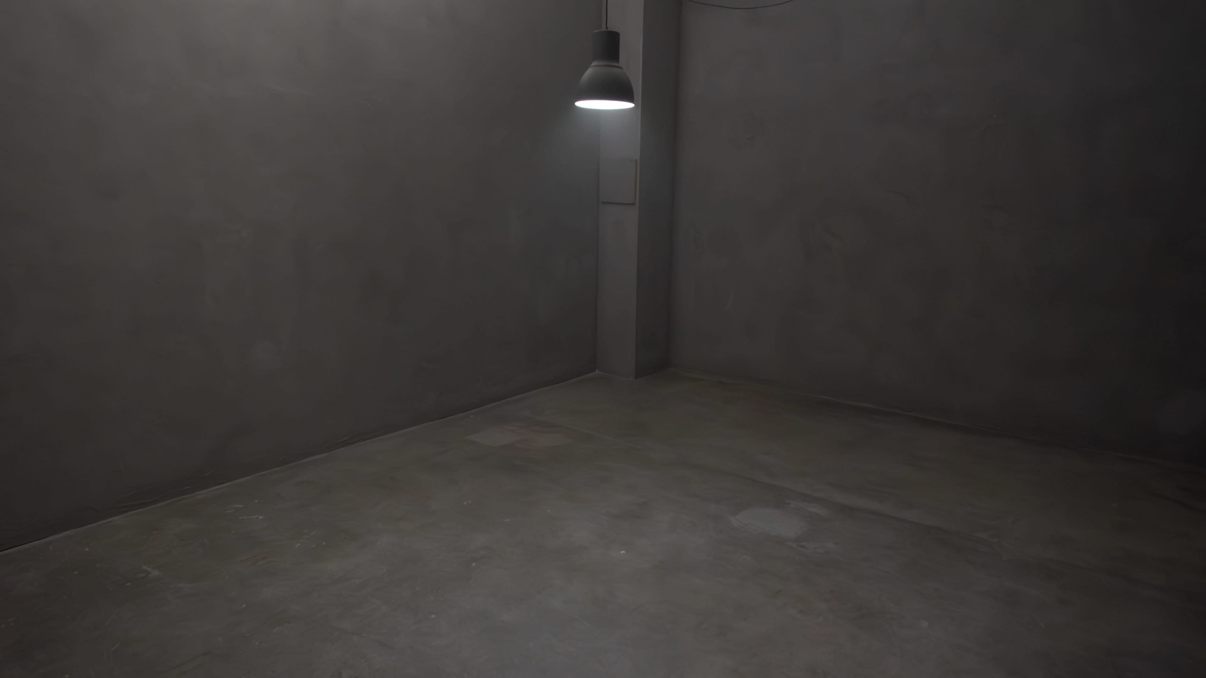 A dimly lit, empty room with gray concrete walls and floor.
