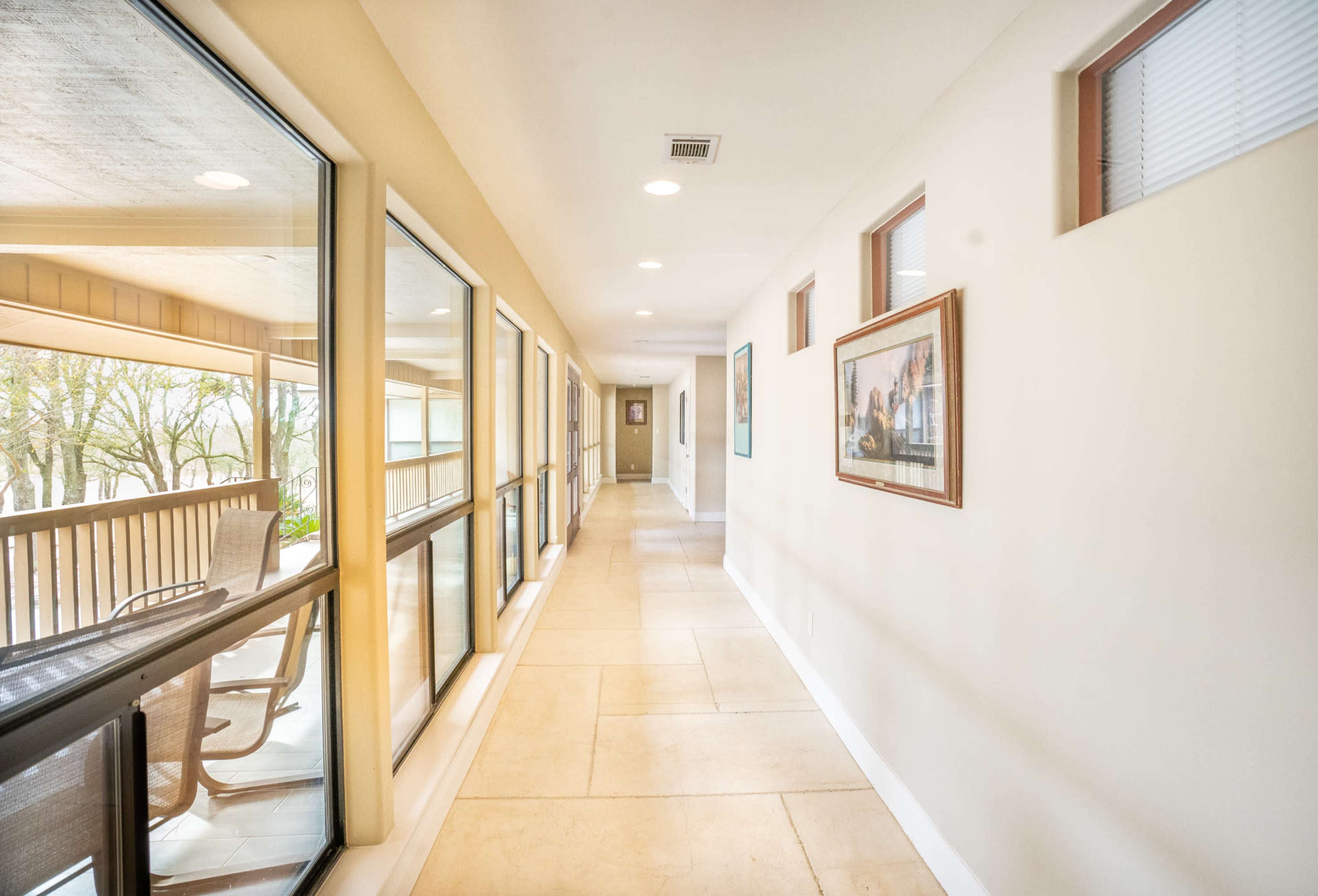 A brightly lit indoor corridor with large windows on one side and framed pictures on the walls.