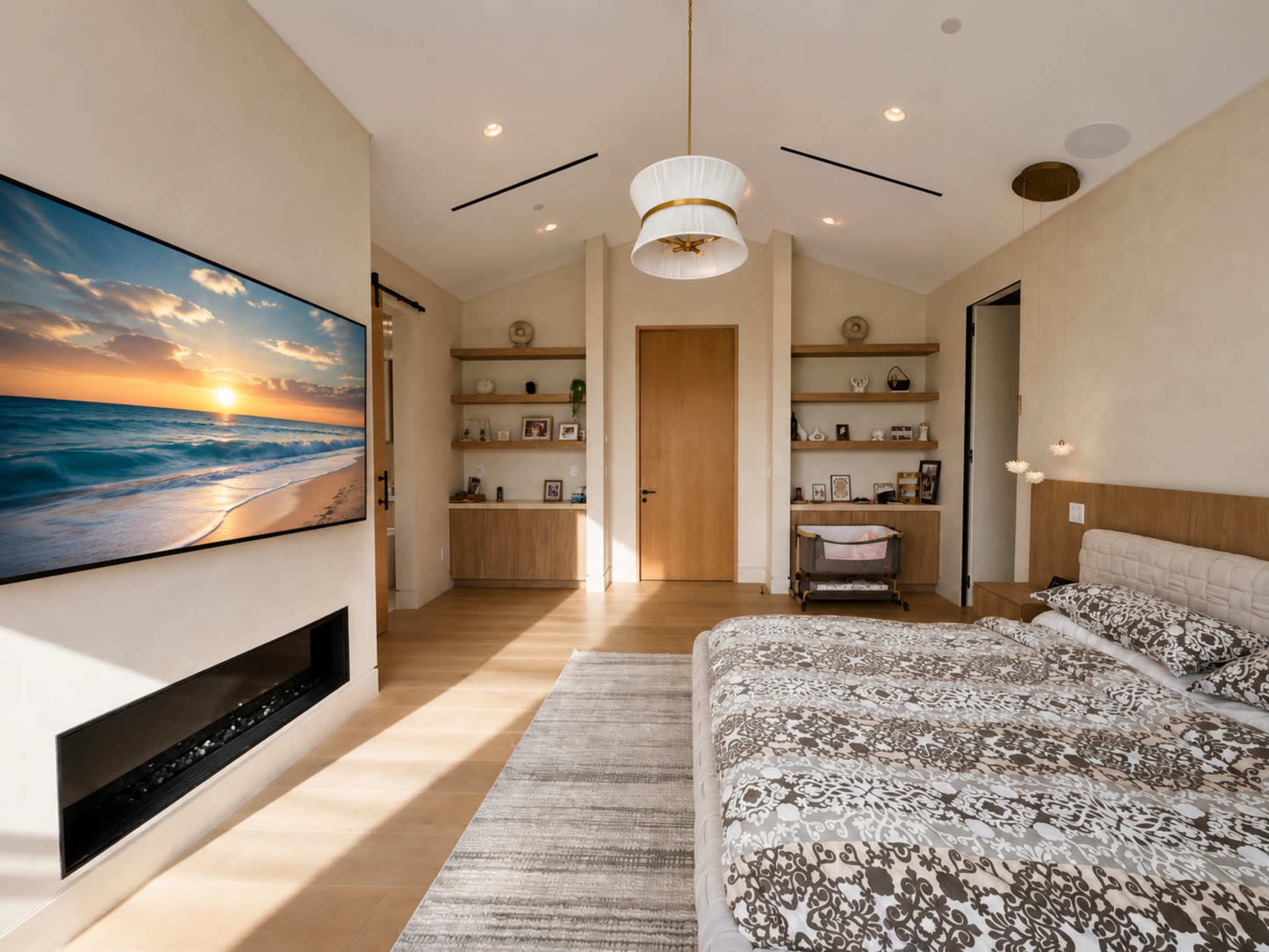 The image shows a modern bedroom with a large bed, a wall-mounted television displaying a sunset over the ocean, and shelves showcasing personal photographs and decor.