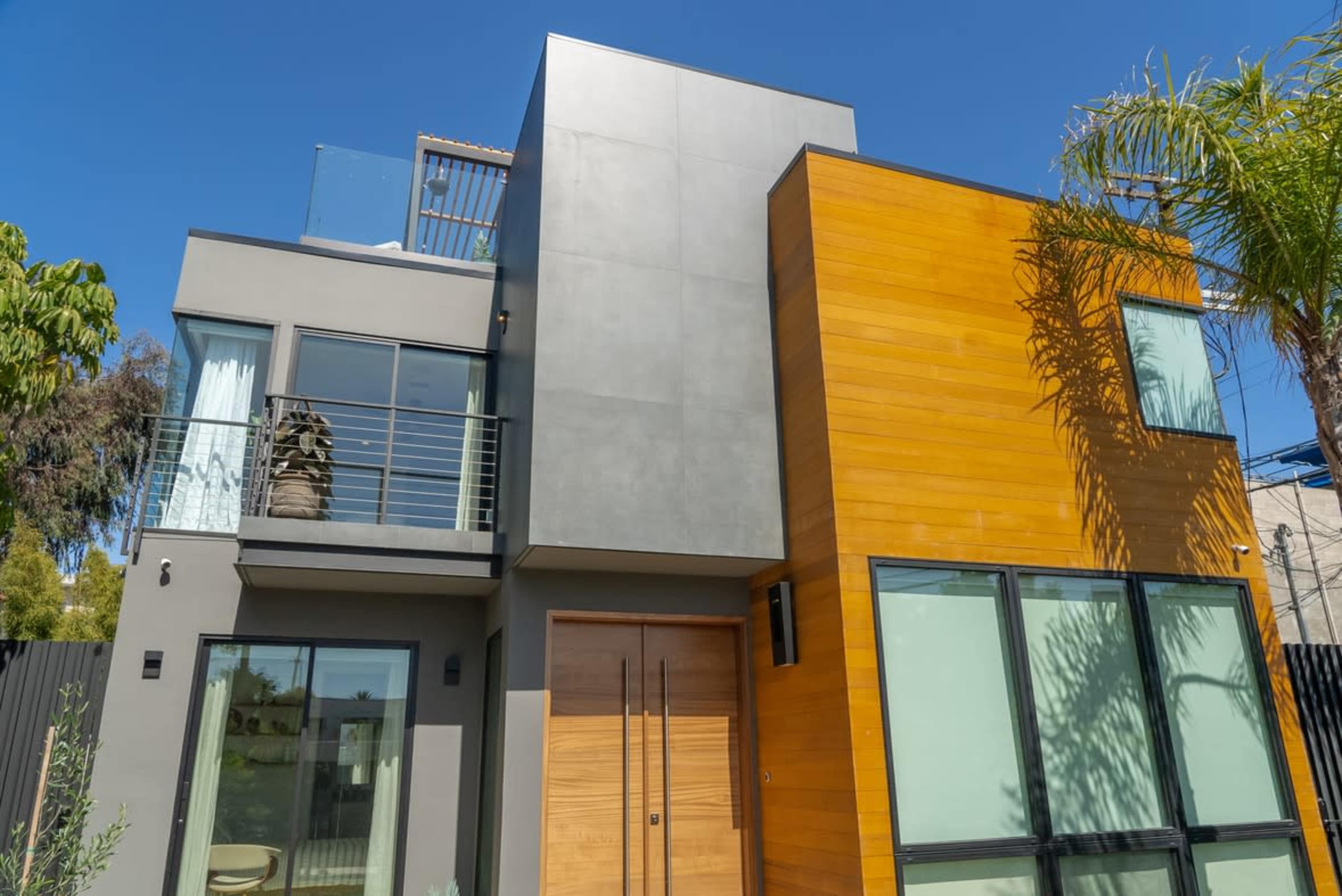 A modern two-story house with a combination of gray and wooden exterior walls, large windows, and a rooftop terrace.