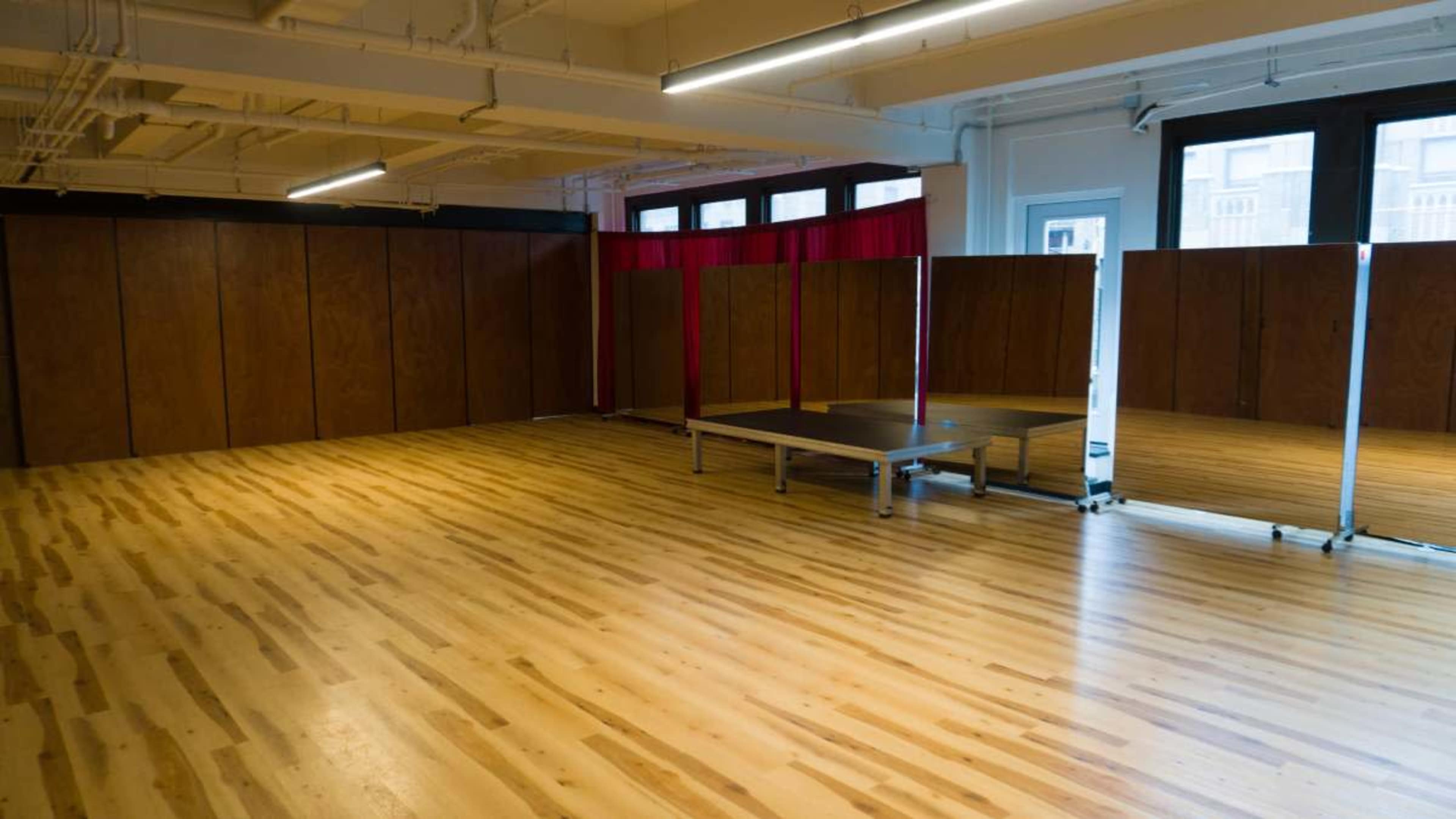 The image shows a spacious, empty room with wooden flooring and large wooden partitions separating areas.