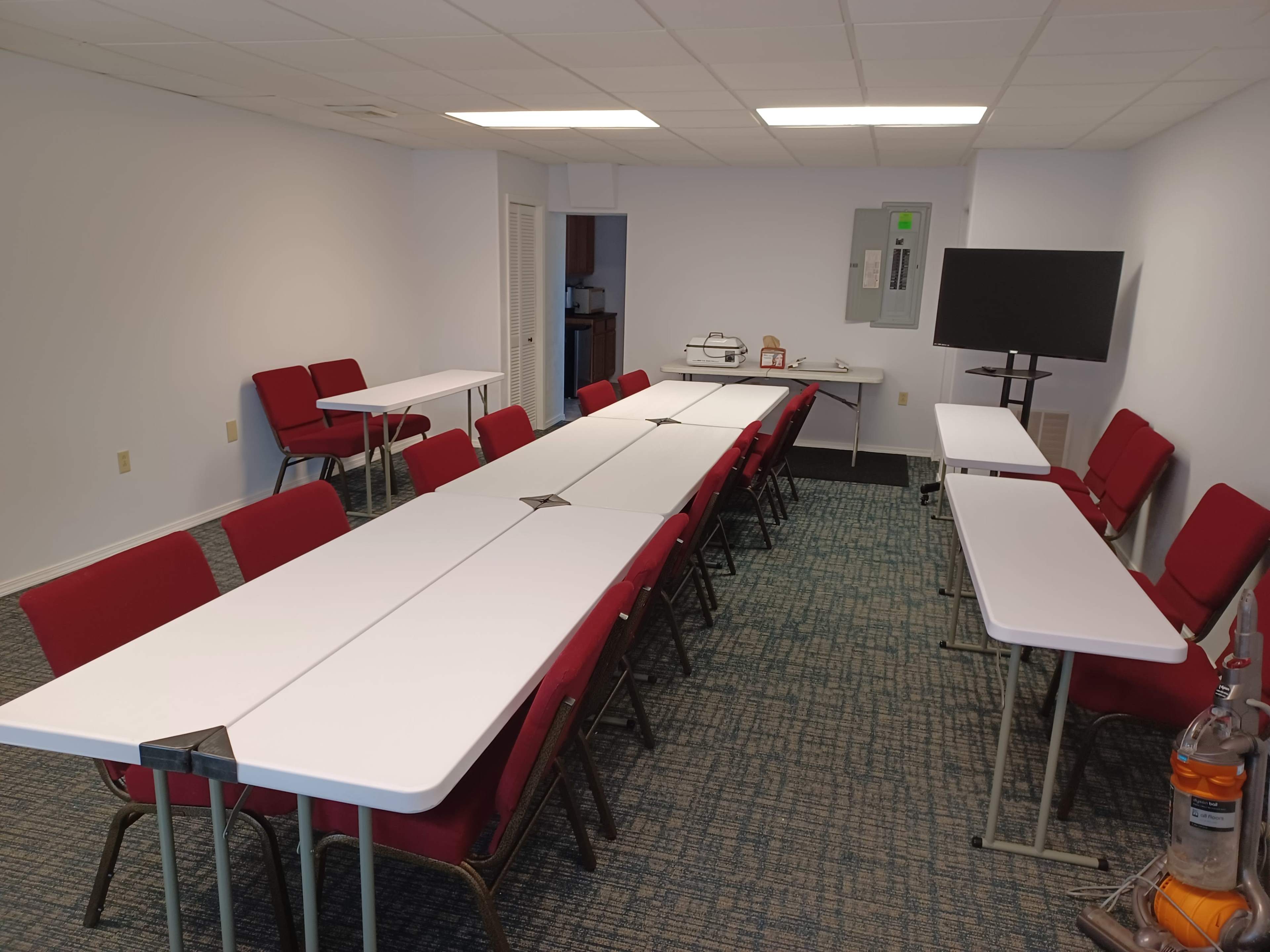 The image shows a conference room with several tables arranged in an extended layout surrounded by red chairs.