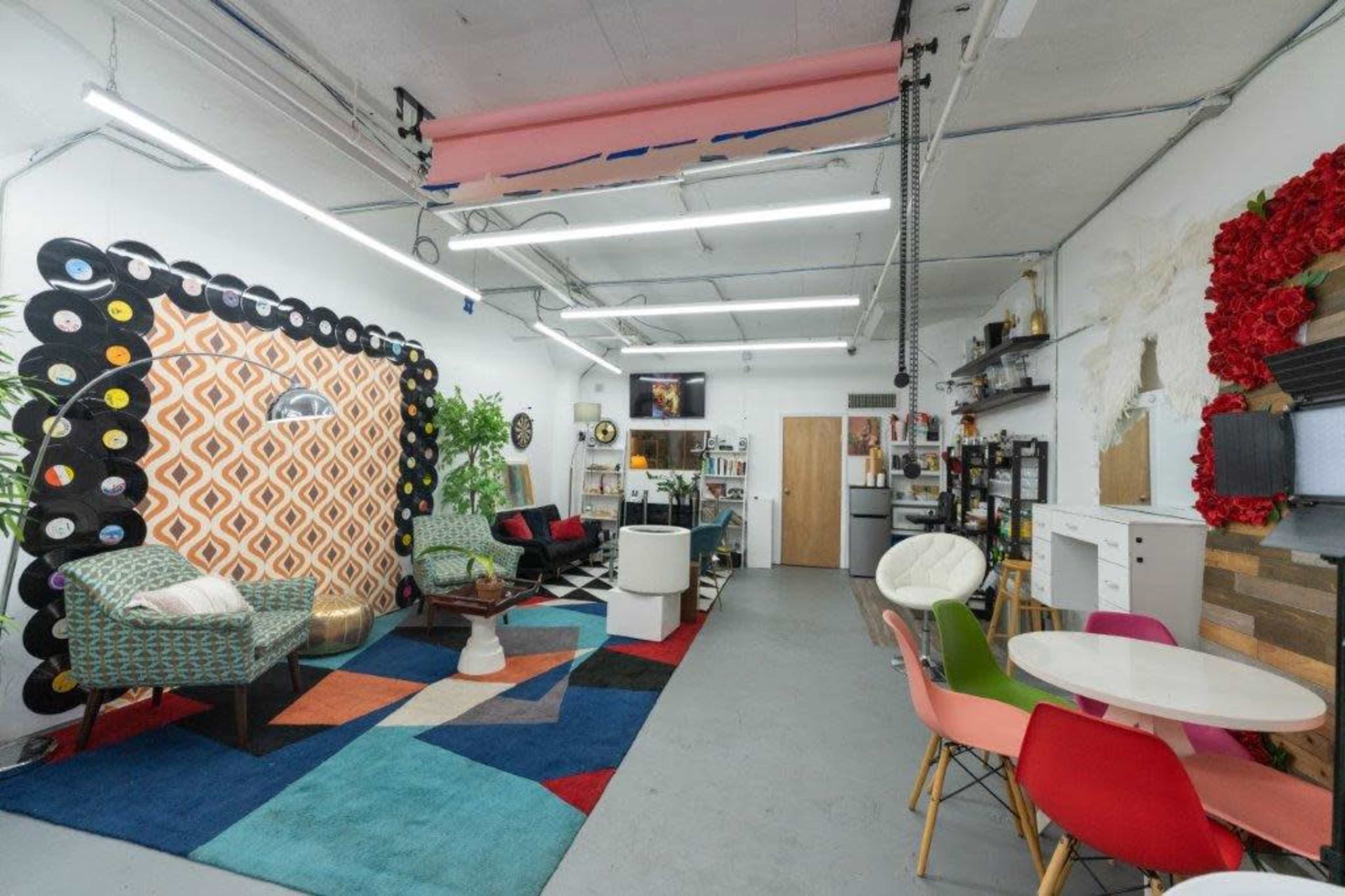 A spacious, modern room with colorful furniture, a patterned rug, and decorative wall accents featuring vinyl records and flowers.