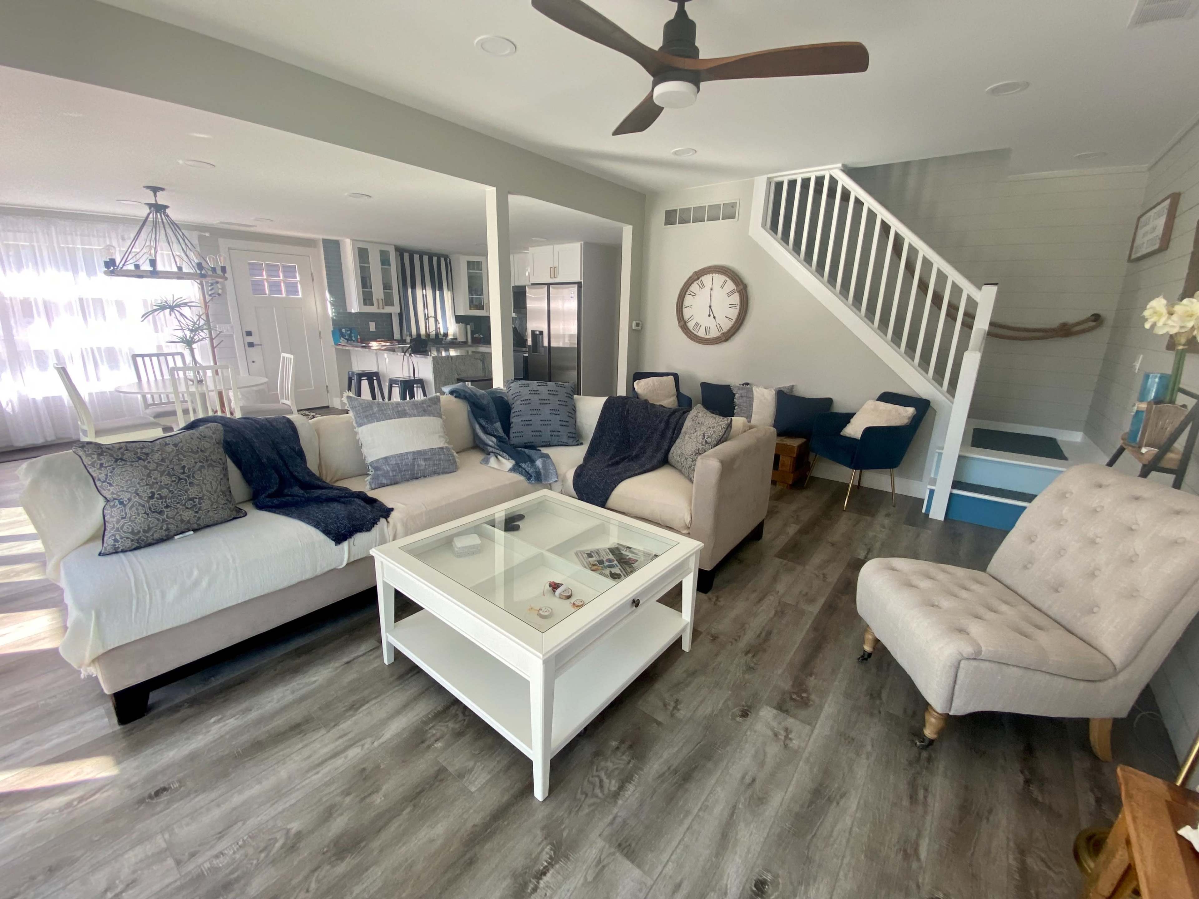 A modern living room with a sectional sofa, a glass-top coffee table, and a staircase in the background.