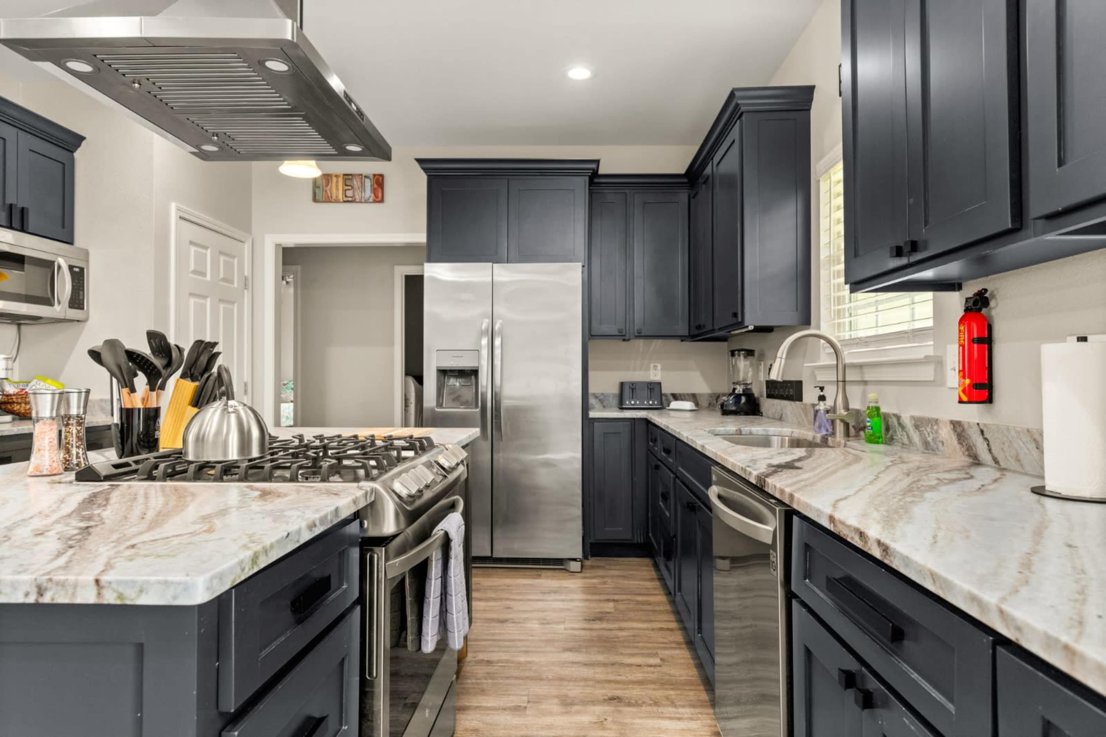 A modern kitchen features dark cabinetry, a large stainless steel refrigerator, and a gas stove with a marble countertop.