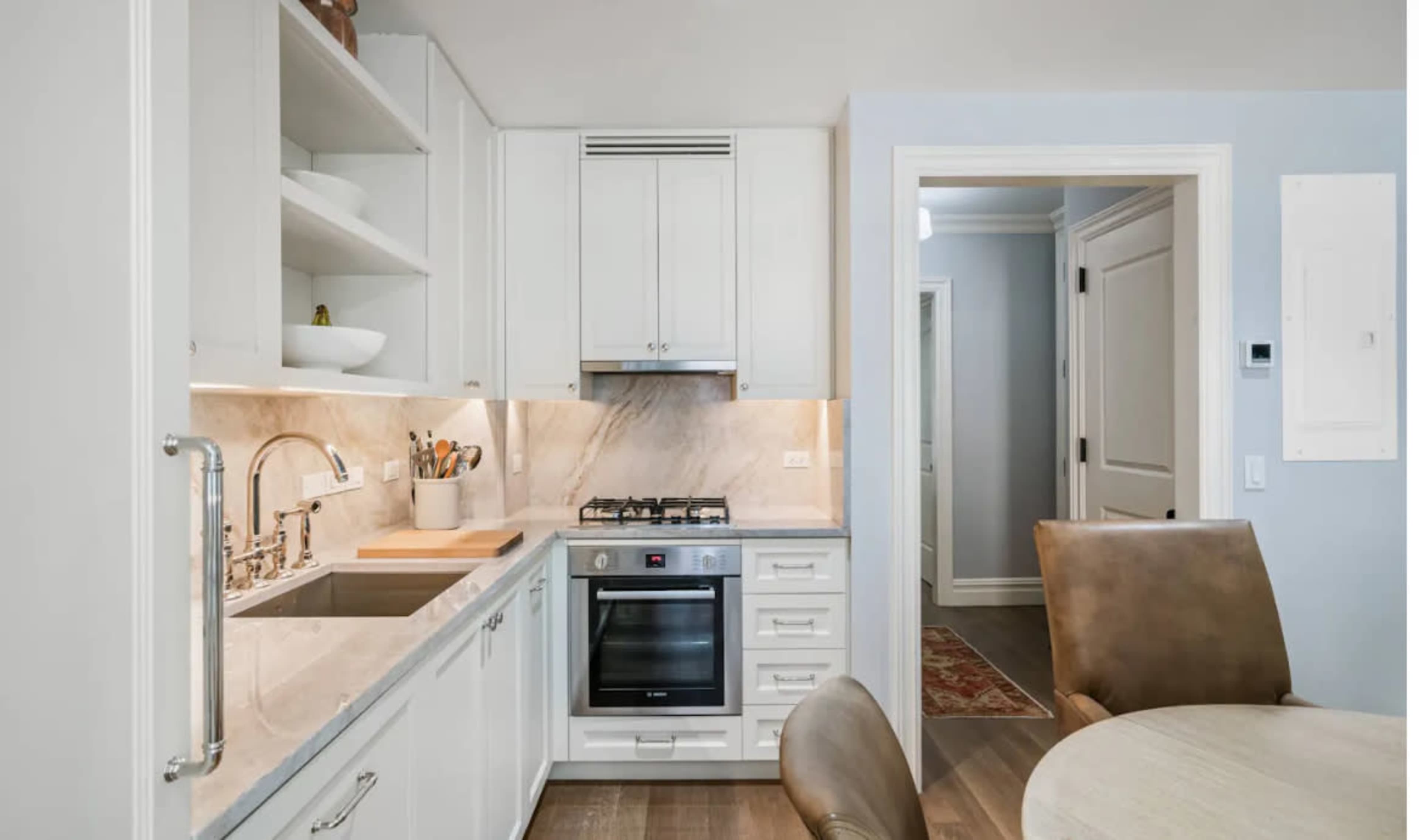 The image shows a modern kitchen featuring white cabinetry, a marble backsplash, a gas stove, and a dining area with a round table and chairs.