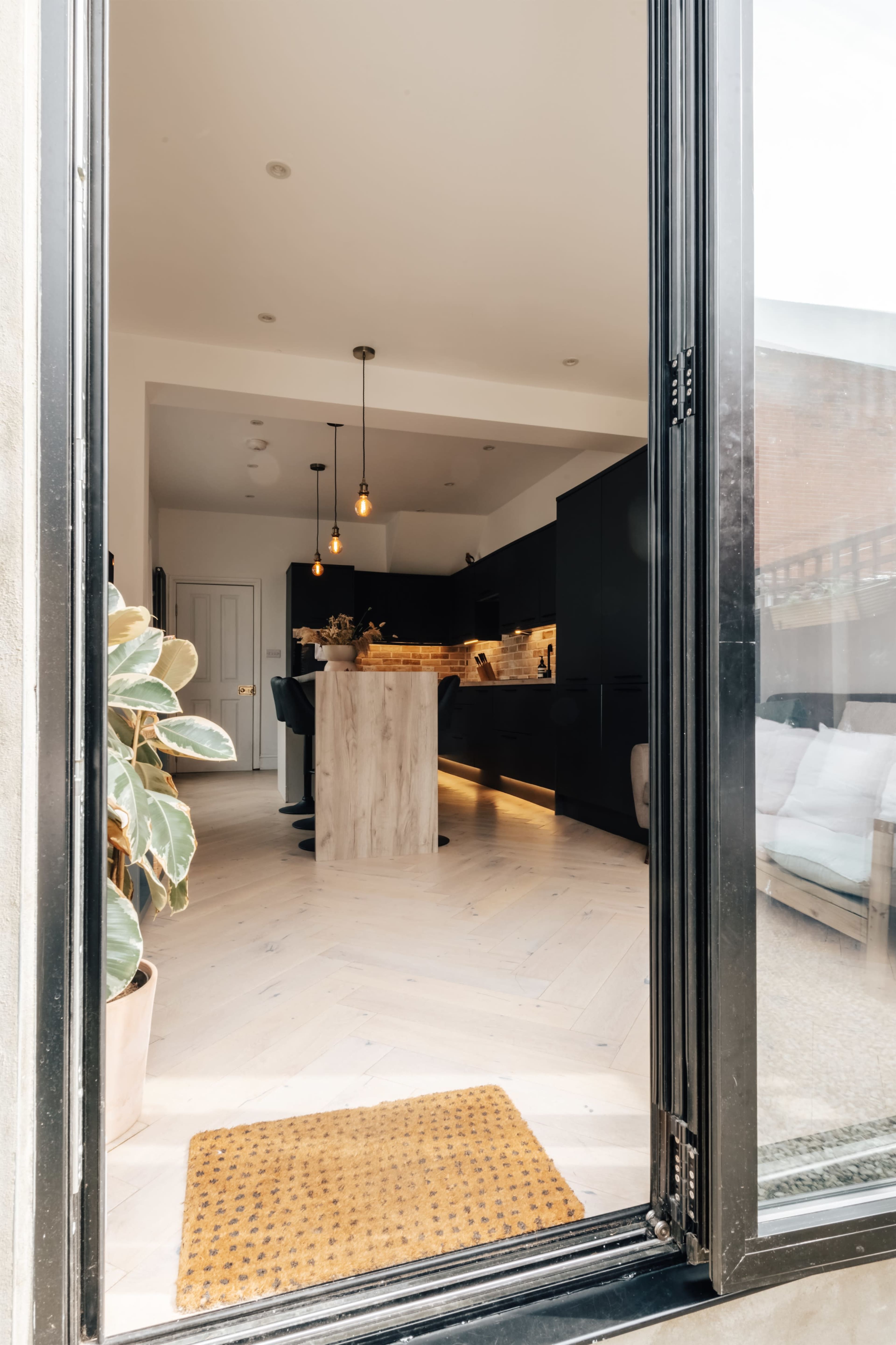 A modern kitchen with black cabinetry and a central island is visible through an open doorway, illuminated by pendant lighting.