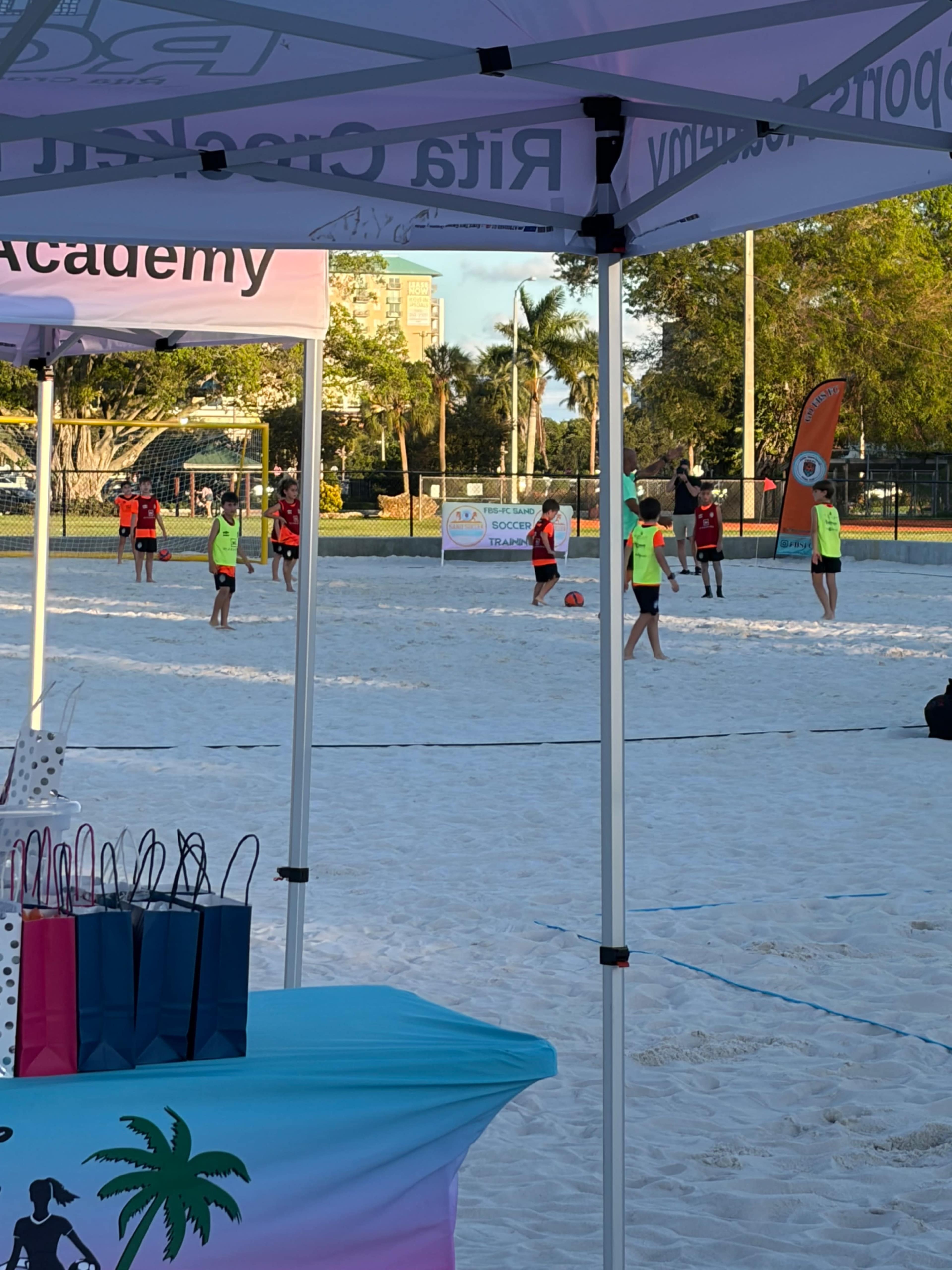 A group of individuals participates in a beach volleyball practice session beneath colorful tents on a sandy court.