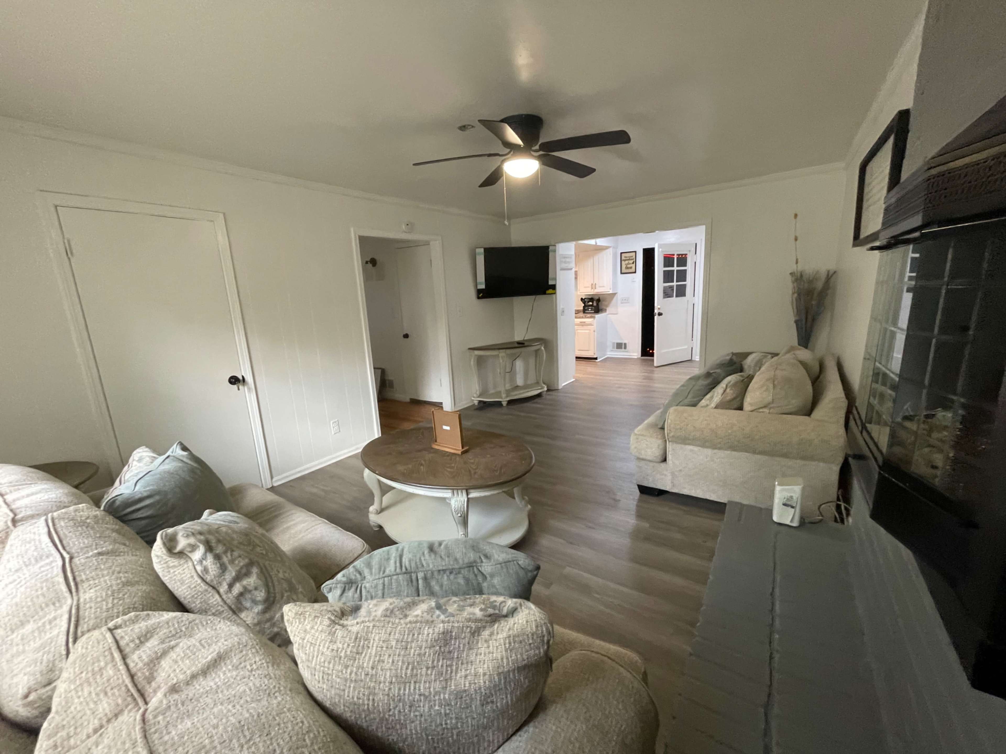 The image shows a living room with a couch, a coffee table, and a view of an adjoining kitchen.