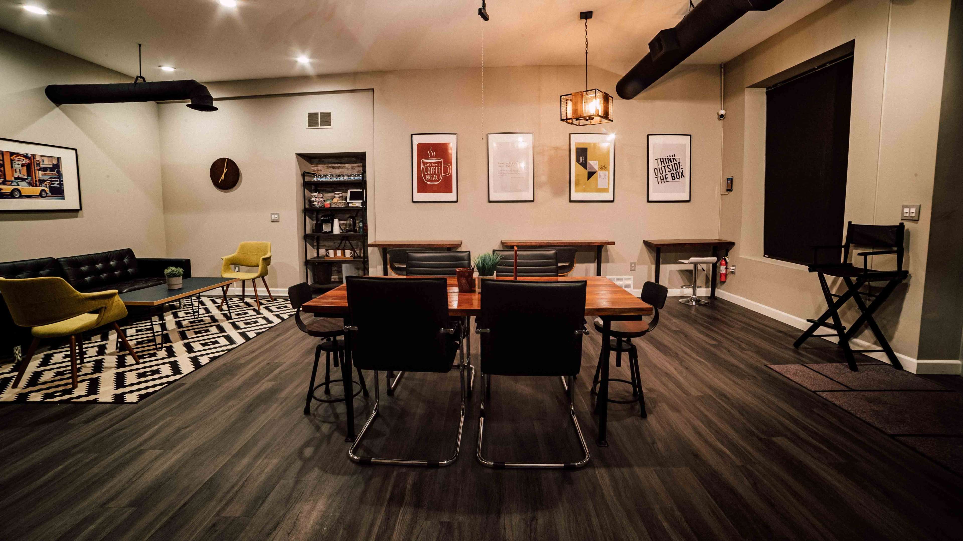 A modern, minimalist interior space featuring a dining table with four chairs, a sofa, and various framed artworks on the walls.