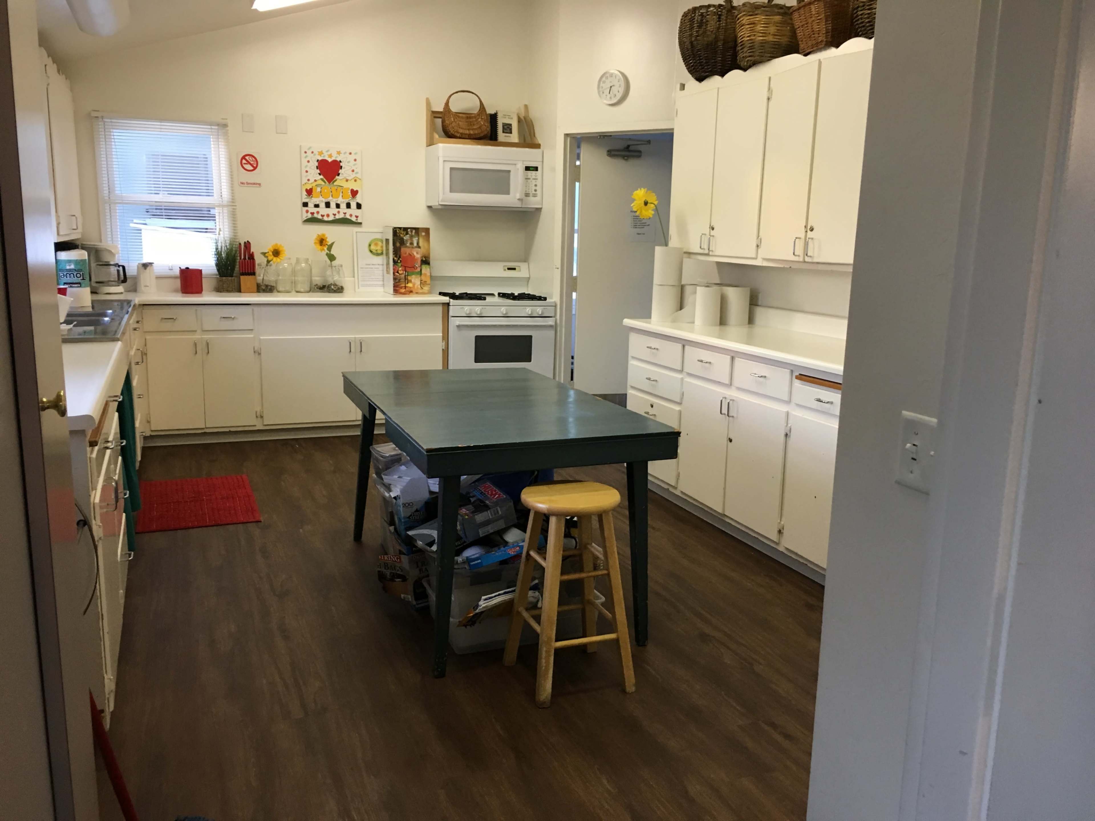 A kitchen featuring white cabinets, a central green table with a stool, and various appliances.