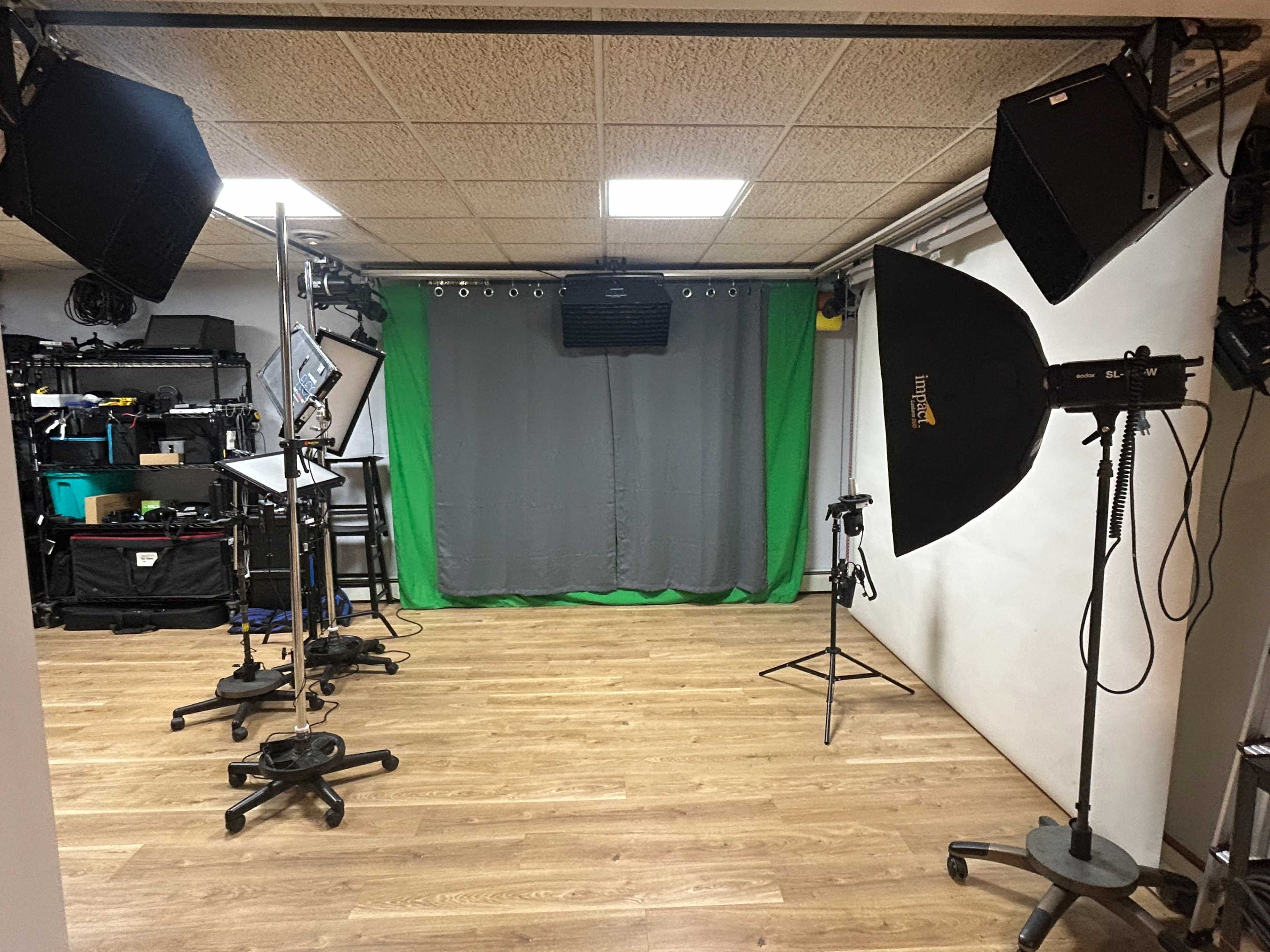 The image shows a photography studio equipped with lighting fixtures, a green backdrop, and various photography equipment arranged around the room.