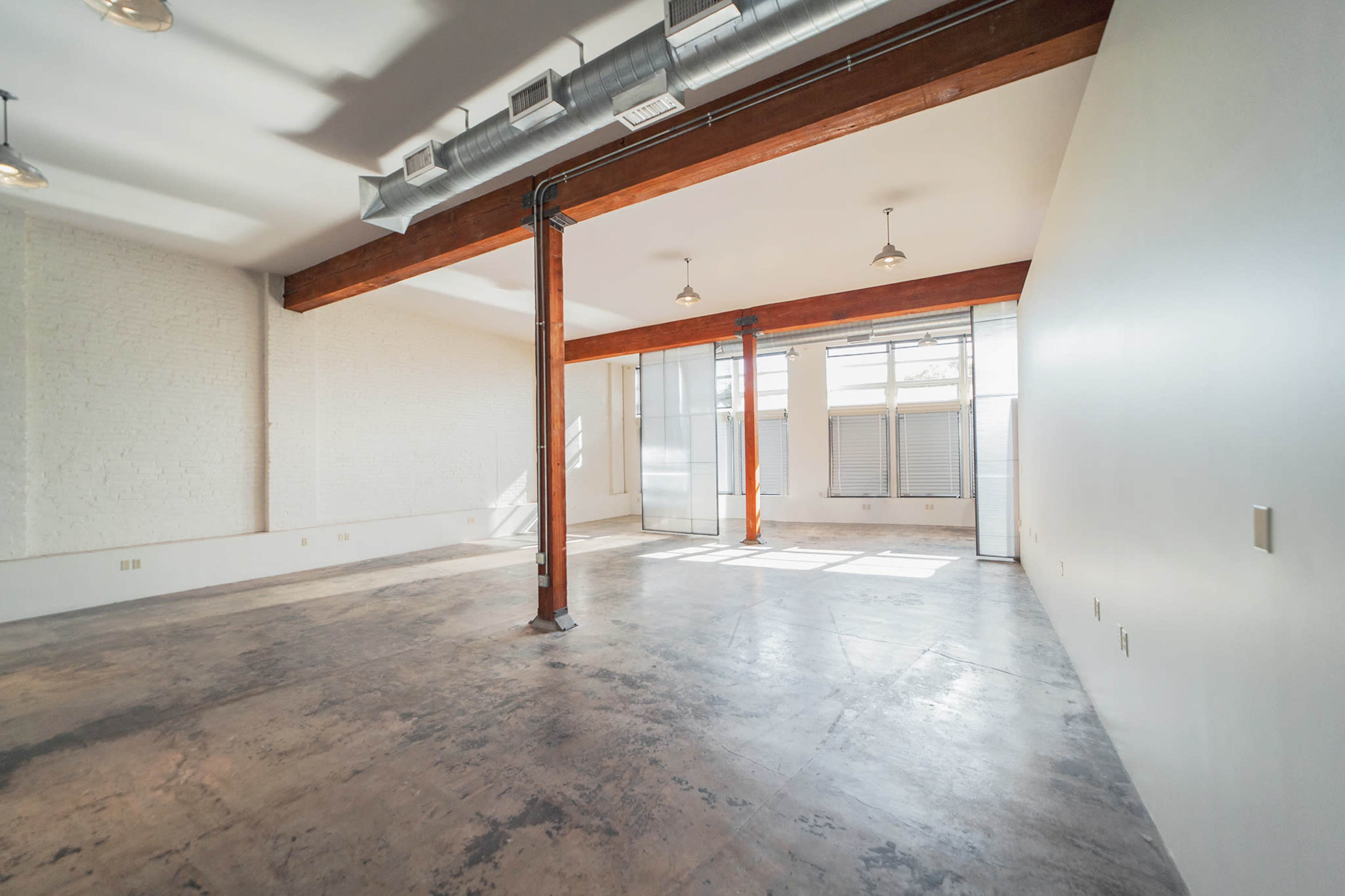 The interior of an empty room features exposed wooden beams and large windows that allow natural light to enter.