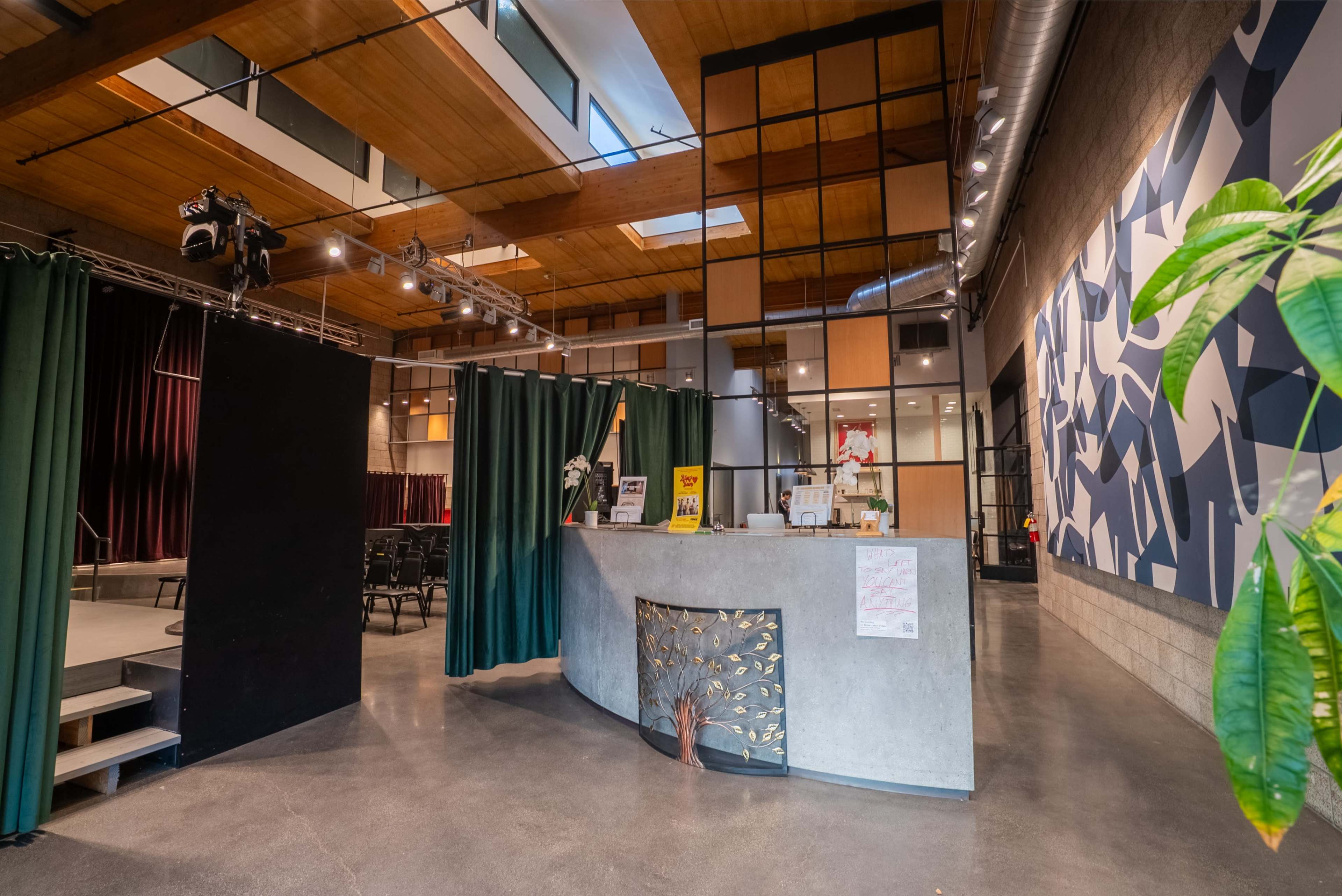 The image shows a modern reception area with a concrete front desk, green curtains, and seating arranged in the background, illuminated by overhead lights.