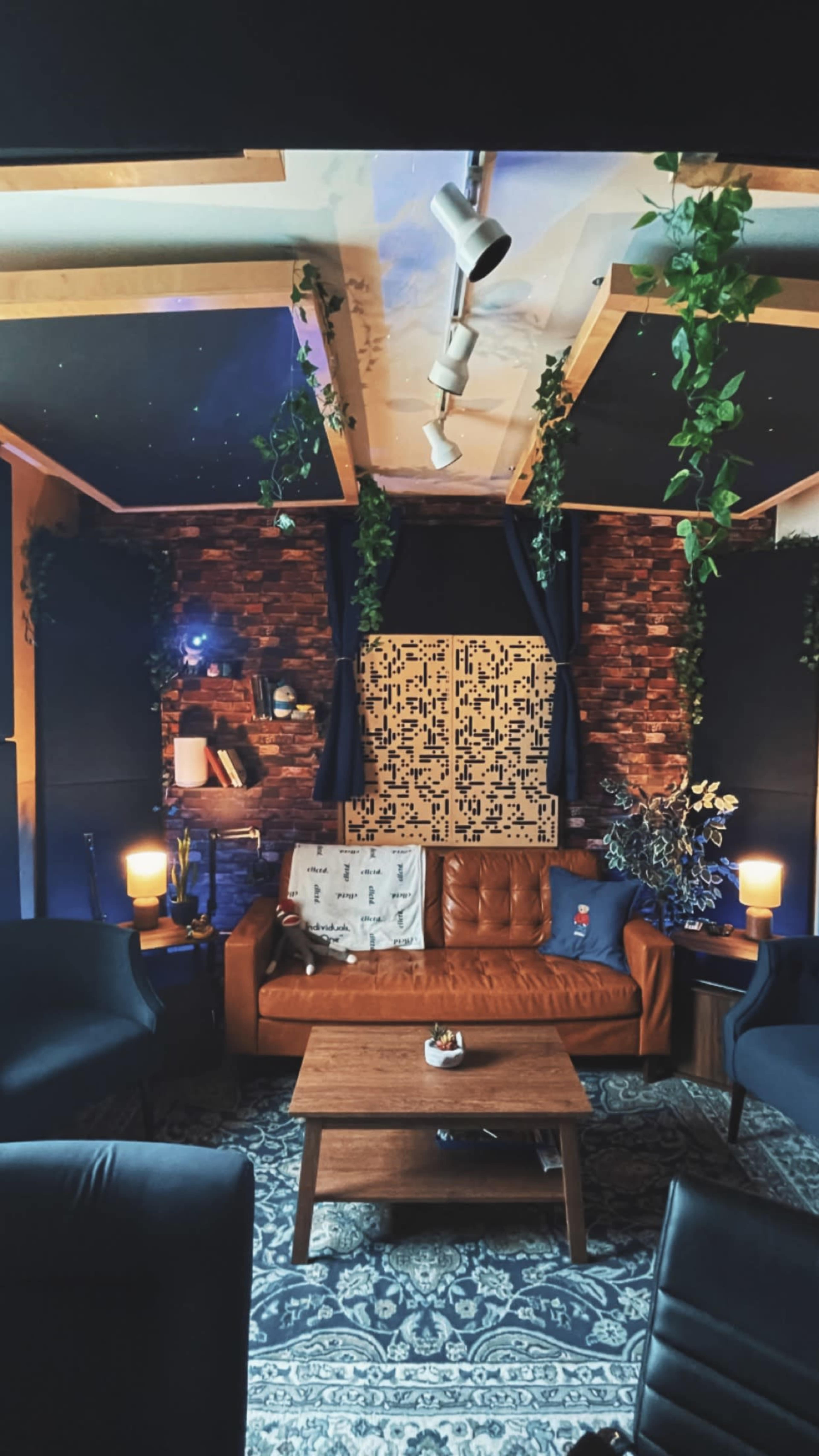 A cozy lounge area with a brown leather sofa, a wooden coffee table, and plants along the walls, illuminated by soft lighting.