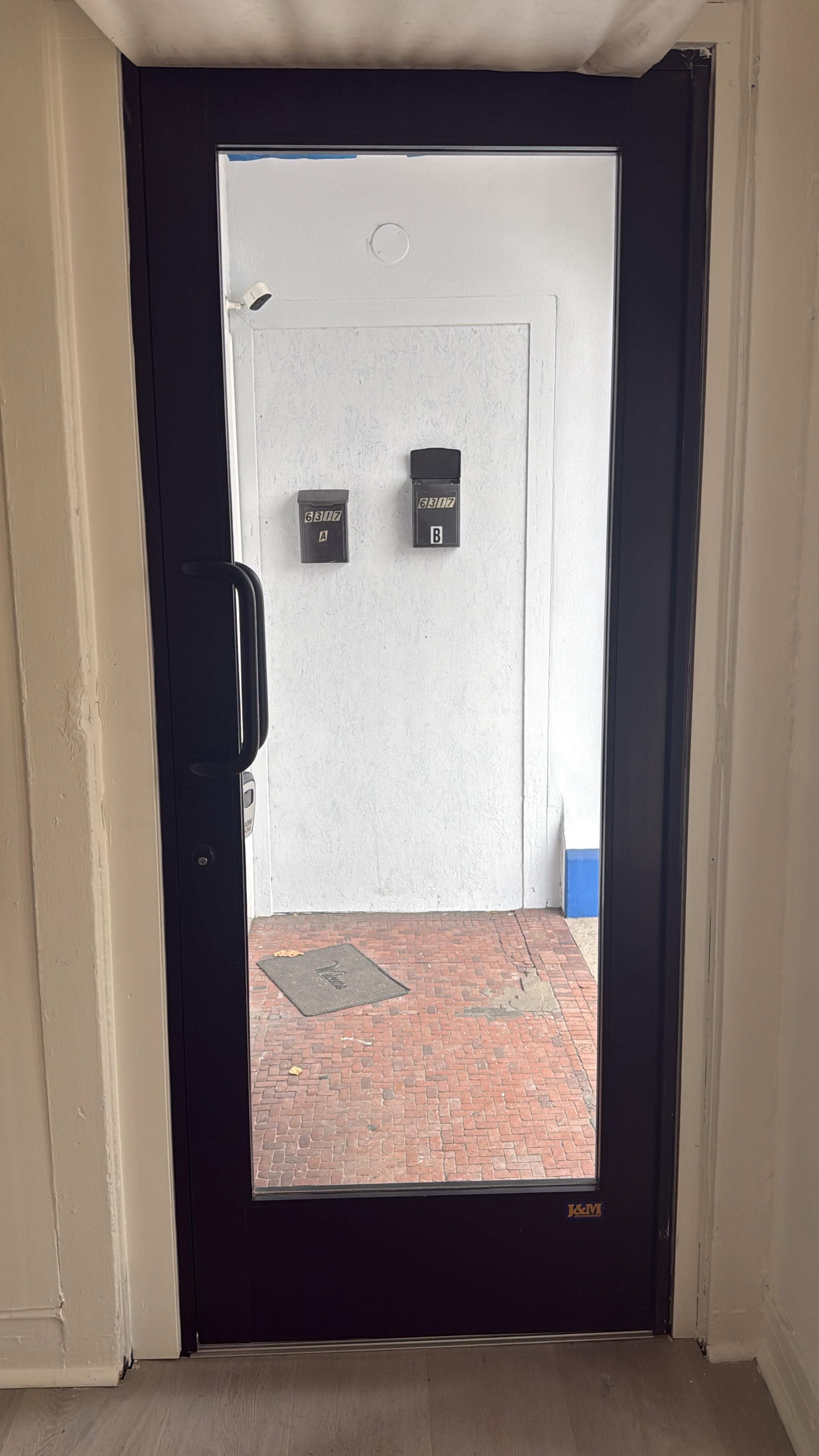 A black-framed glass door reveals a small entryway with two mailboxes on the wall opposite the door.