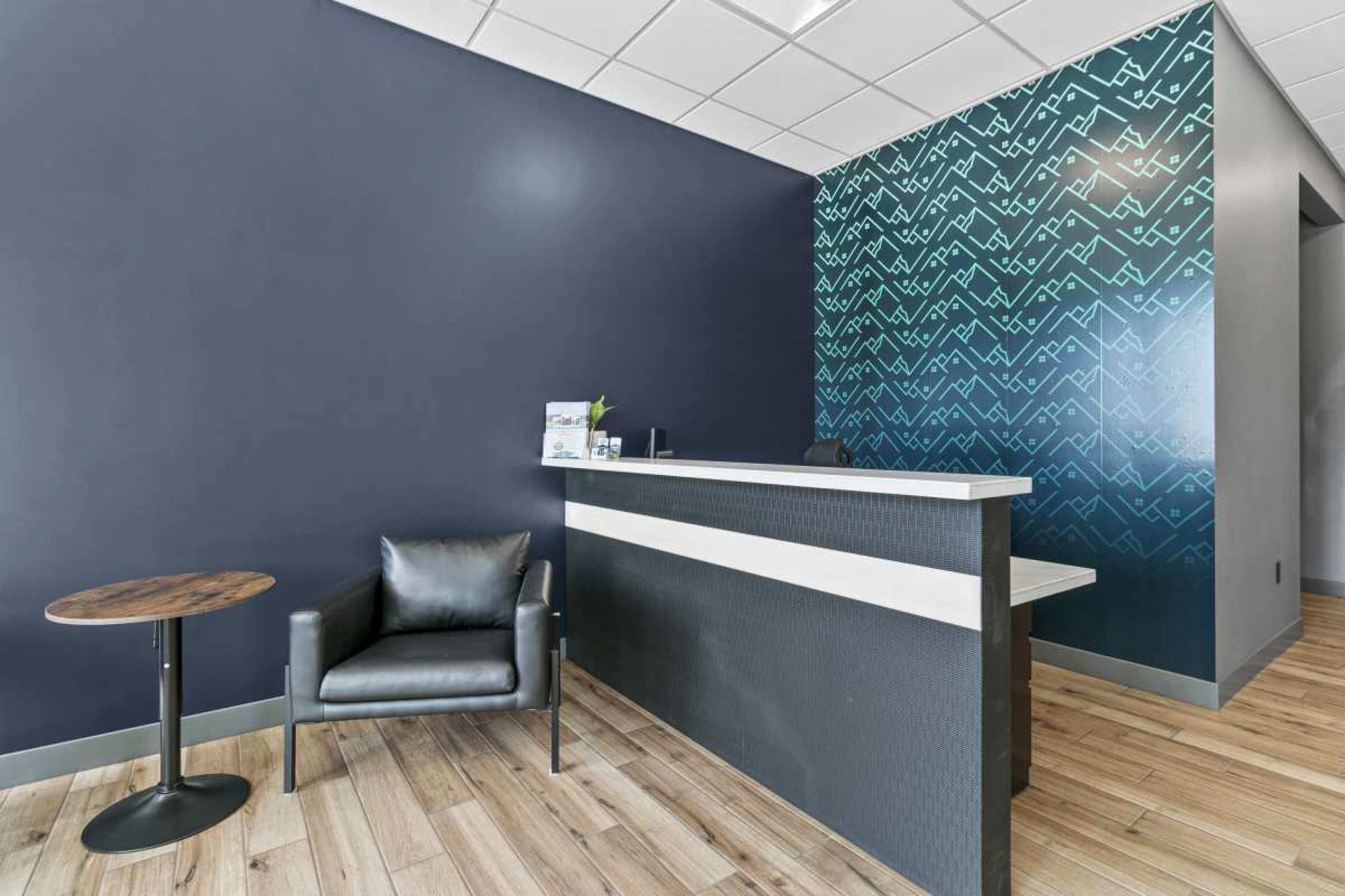 The image shows a modern reception area with a dark blue wall, a patterned accent wall, a sleek reception desk, a black chair, and a small round table.