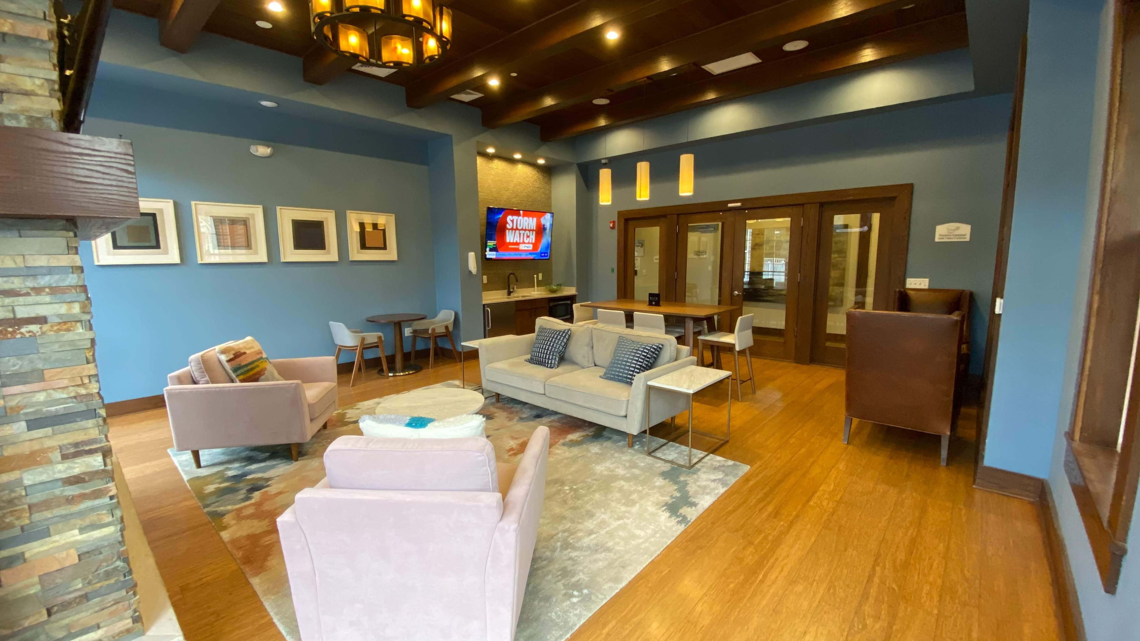 A cozy lounge area with two sofas, a television on the wall, and multiple seating arrangements, all set within a space featuring wooden beams and a stone fireplace.