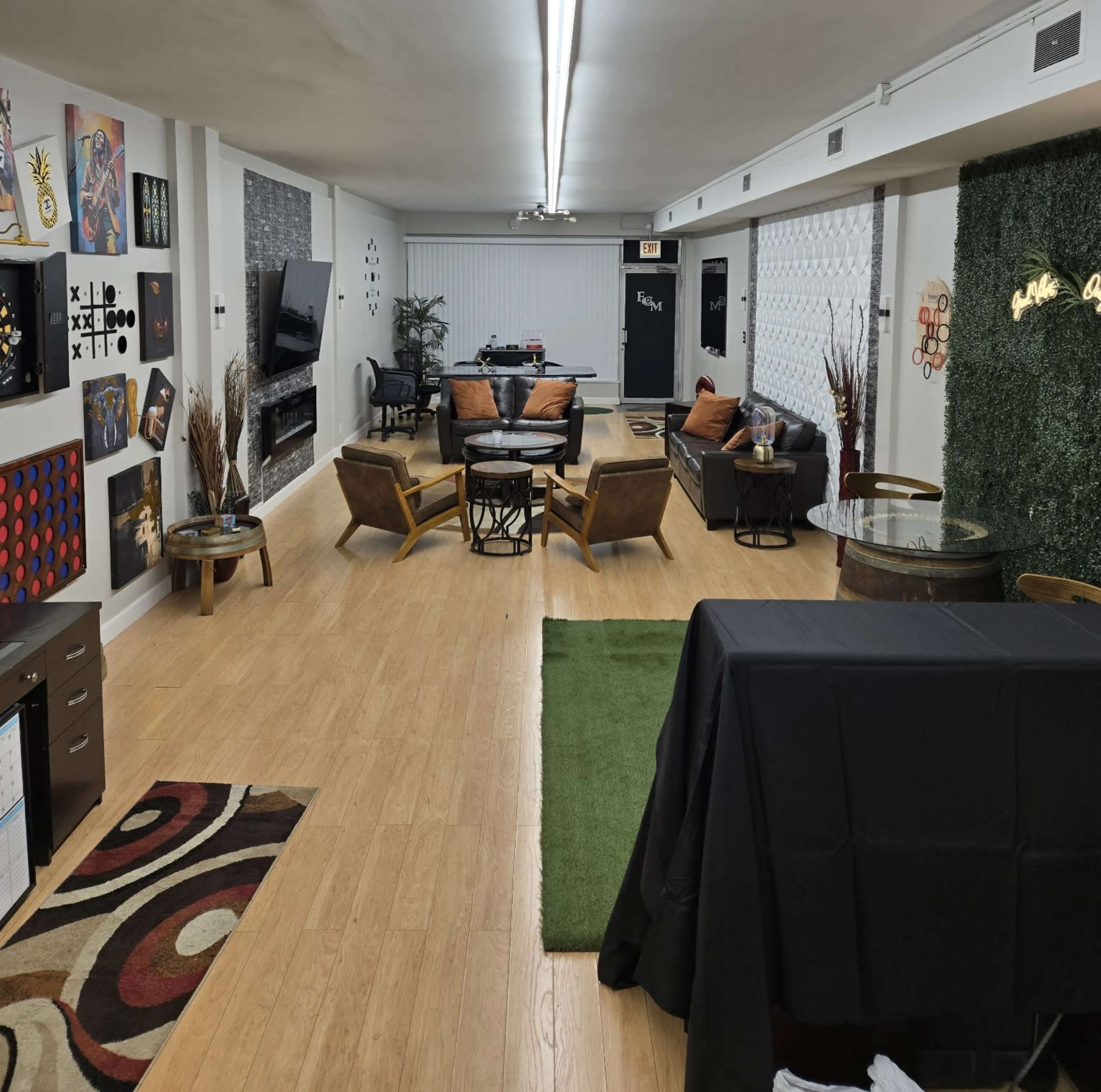 The image shows a spacious, well-furnished lounge area with seating arrangements, decorative wall art, and a green grass rug.