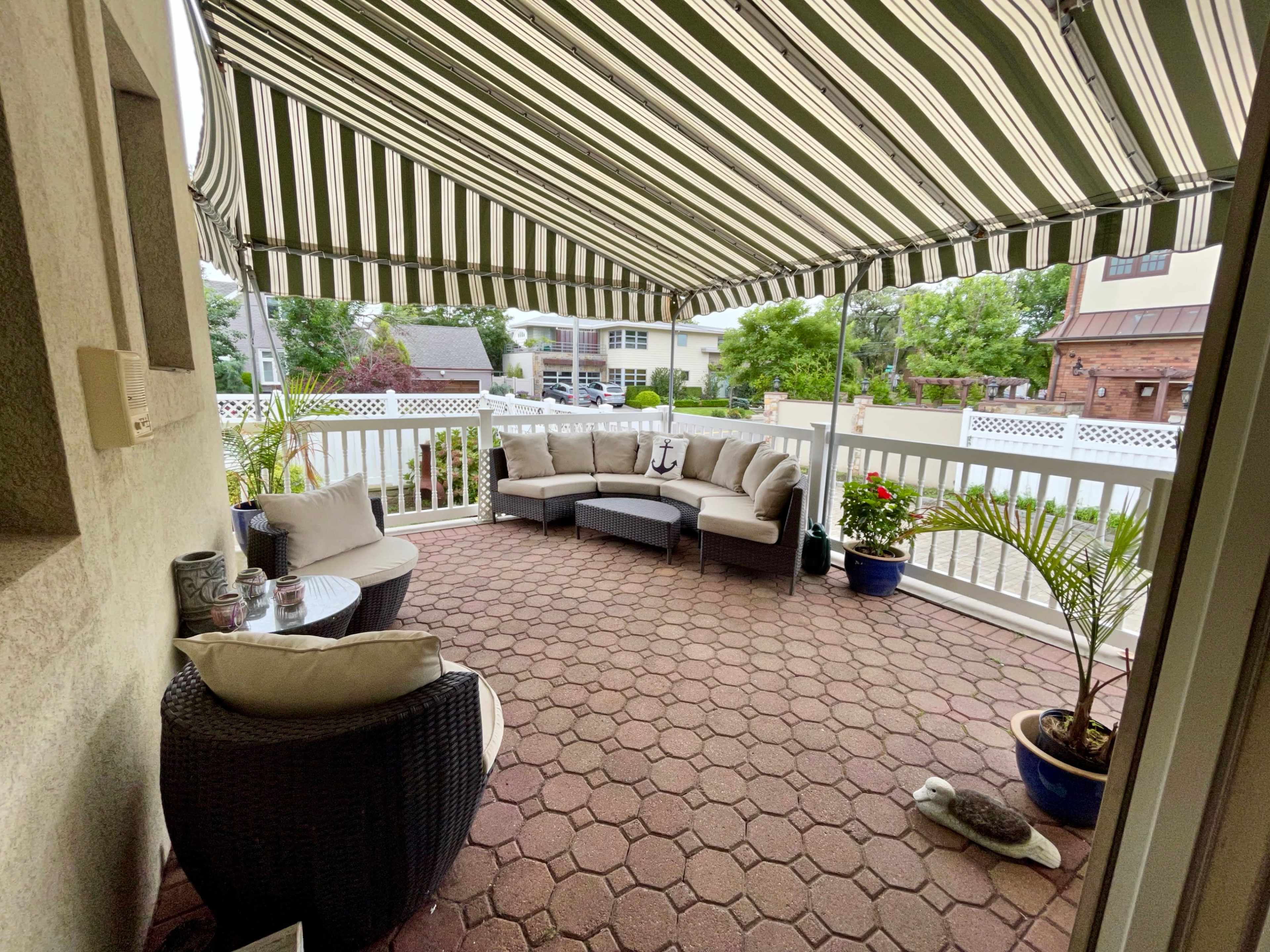 A covered patio with a striped awning, featuring a seating arrangement and potted plants.