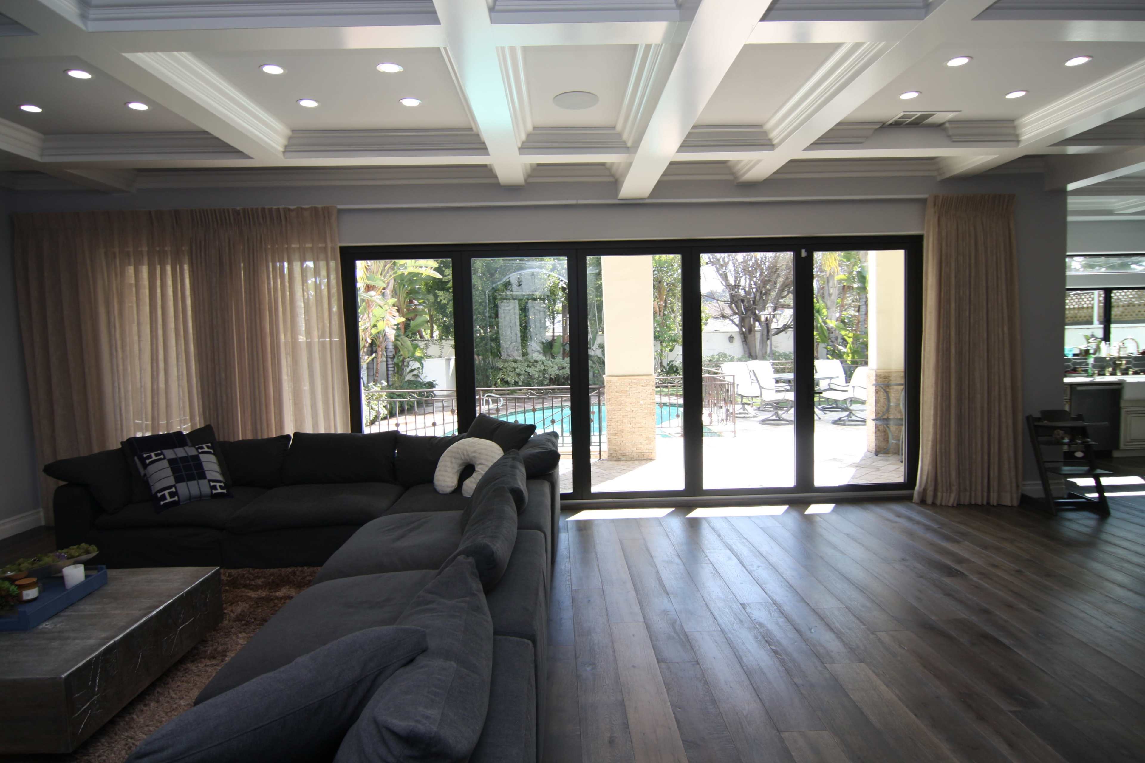 A spacious living room features a large gray sectional sofa facing sliding glass doors that open to a patio with a swimming pool visible outside.