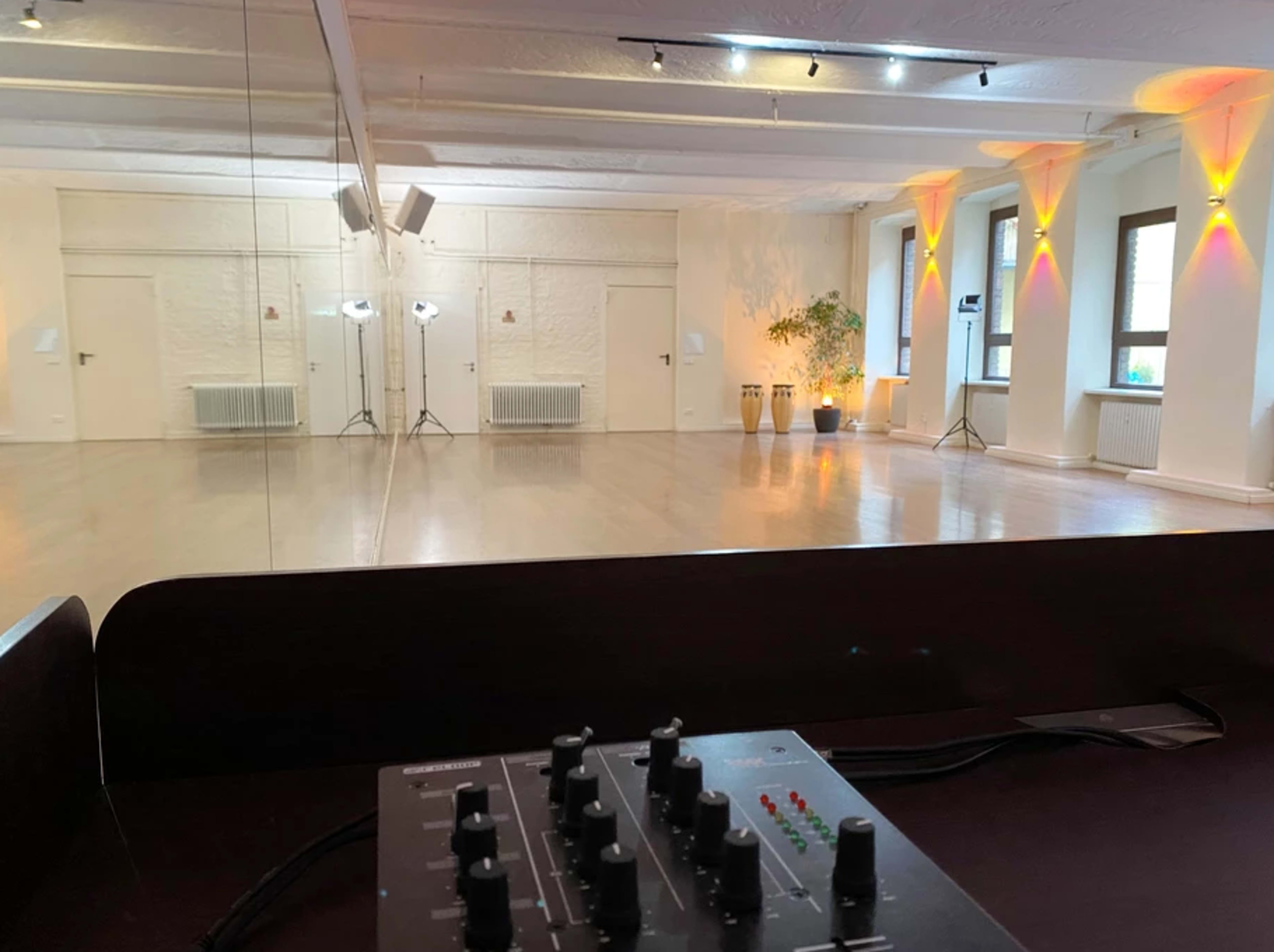 A spacious studio with a polished wooden floor, mirrors on one wall, lighting fixtures, and a sound mixer in the foreground.