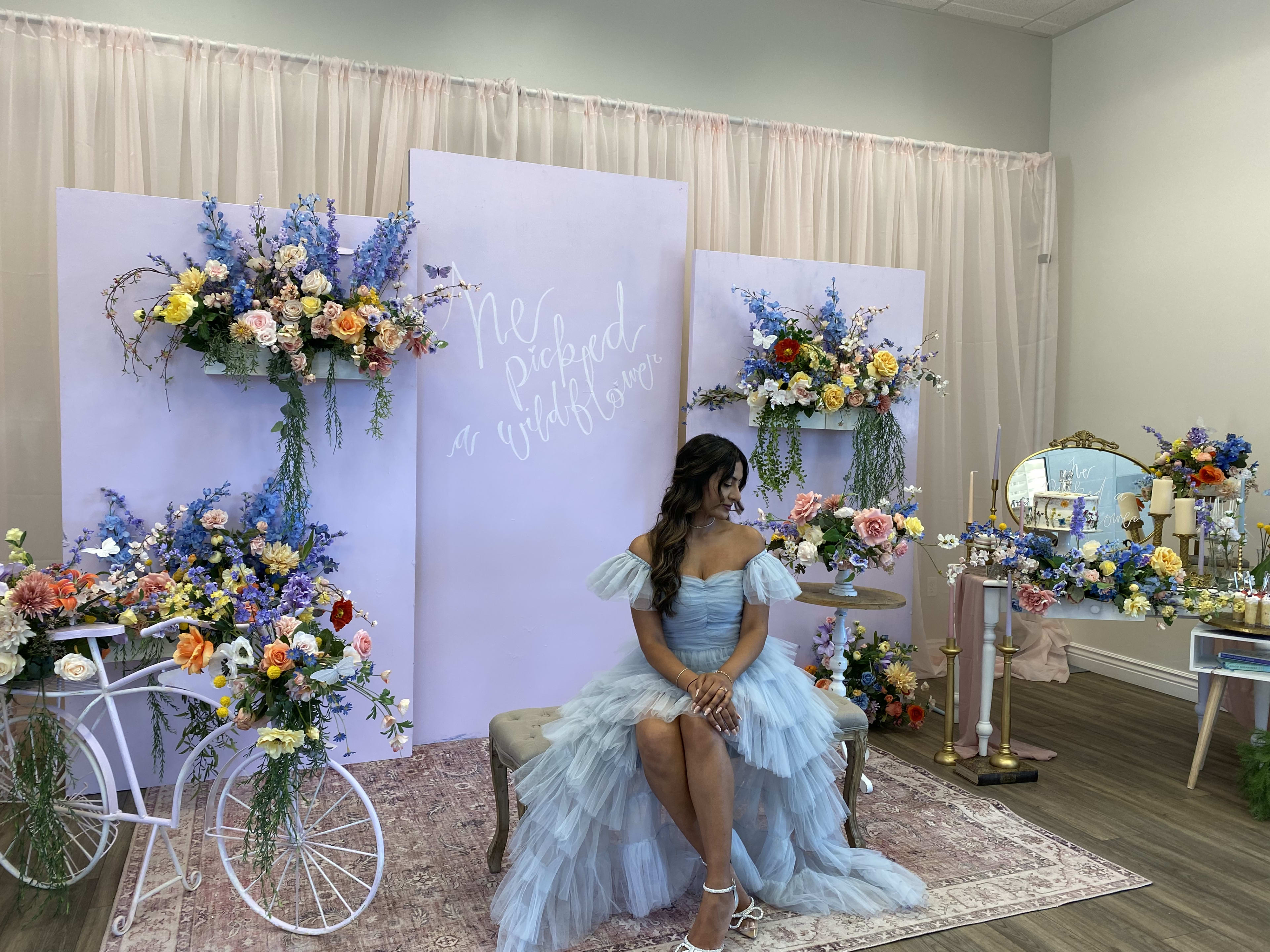 Una futura novia sentada en una silla admirando un jardín de flores moradas y azules para su despedida de soltera en primavera.