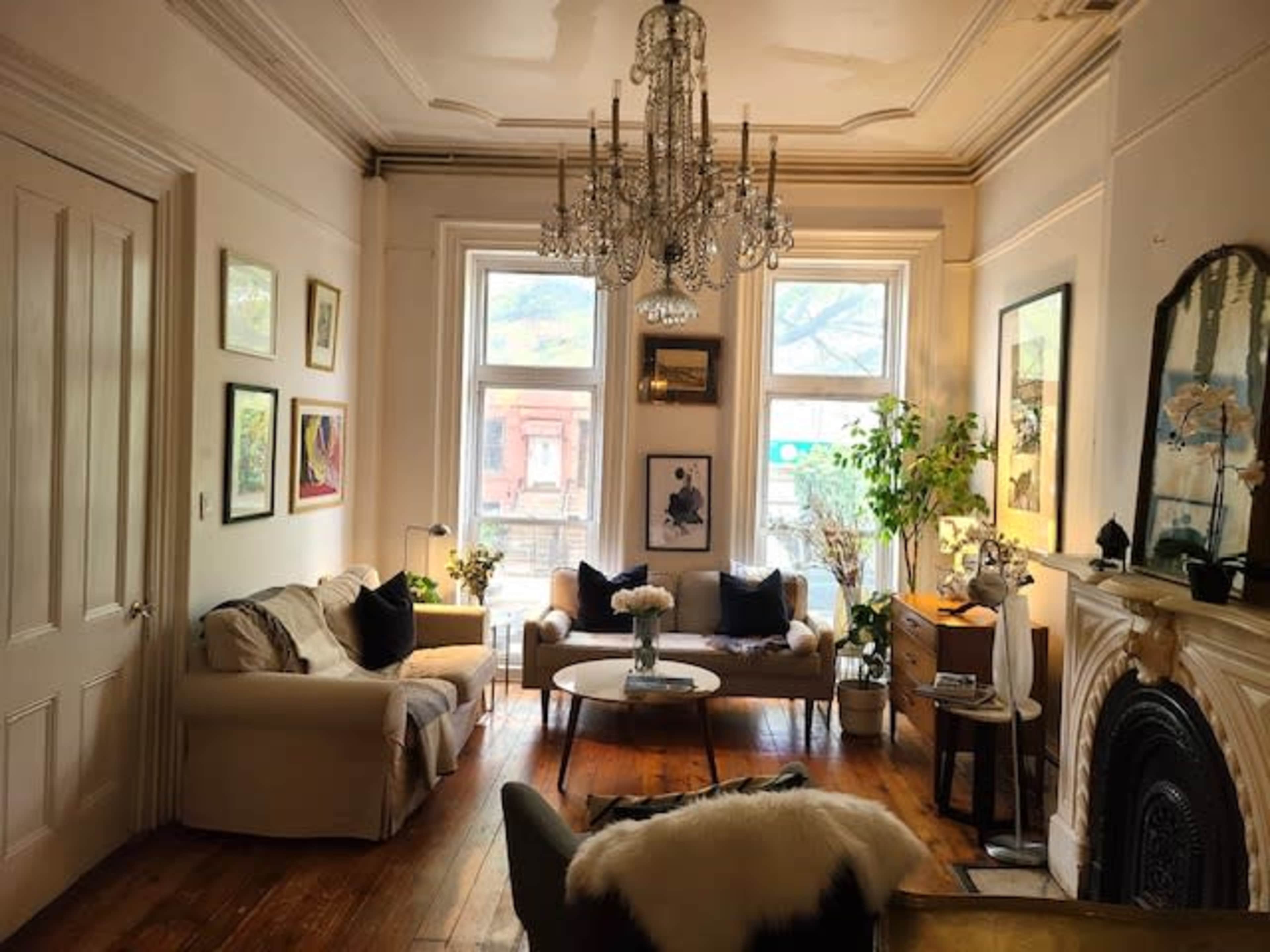 The room features a cozy sitting area with two sofas, a coffee table, a chandelier, and several pieces of artwork on the walls.