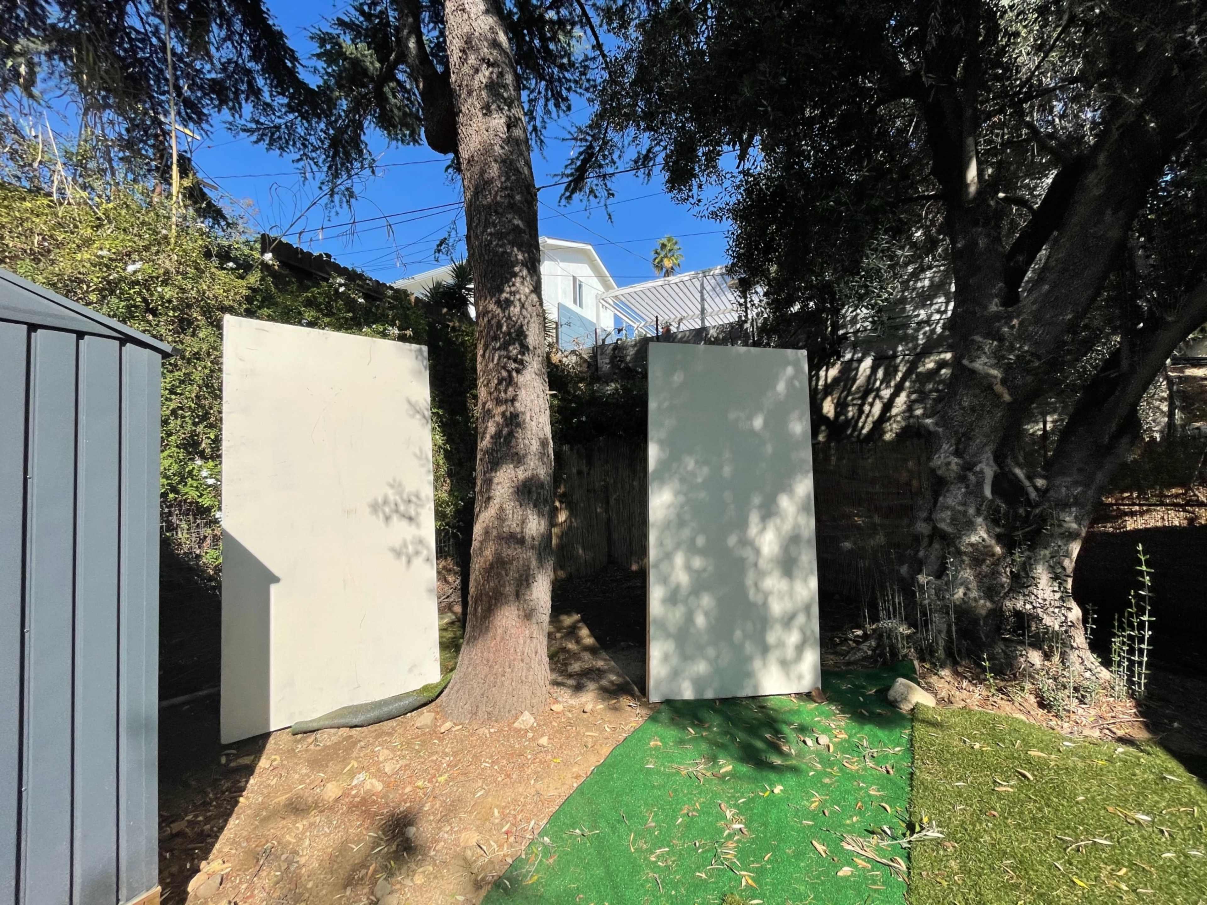 Two large, blank panels stand upright in a backyard surrounded by trees and grass.