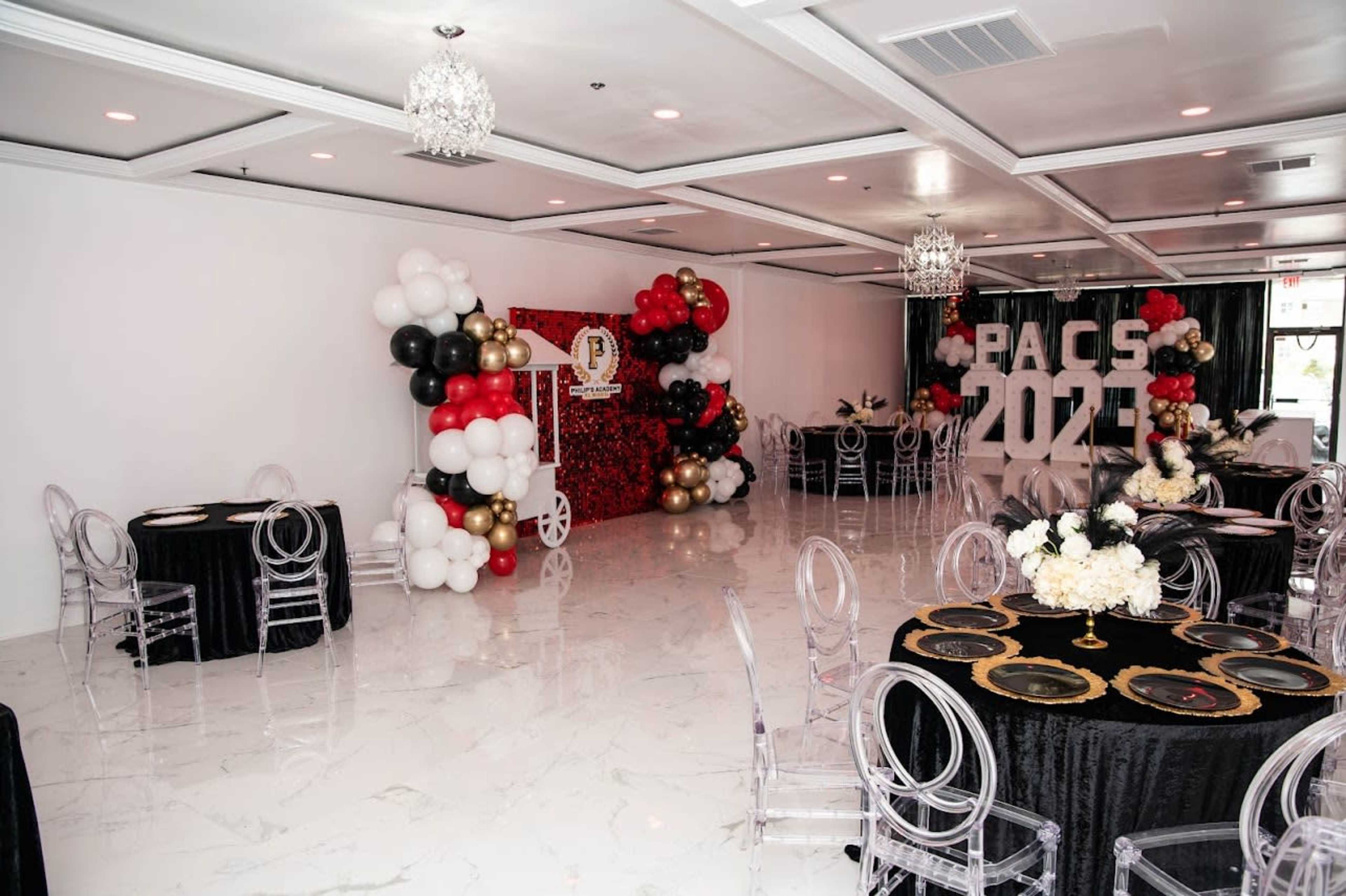 An elegantly decorated event space featuring black and gold tables, a backdrop with balloons, and the year "2023" displayed prominently.