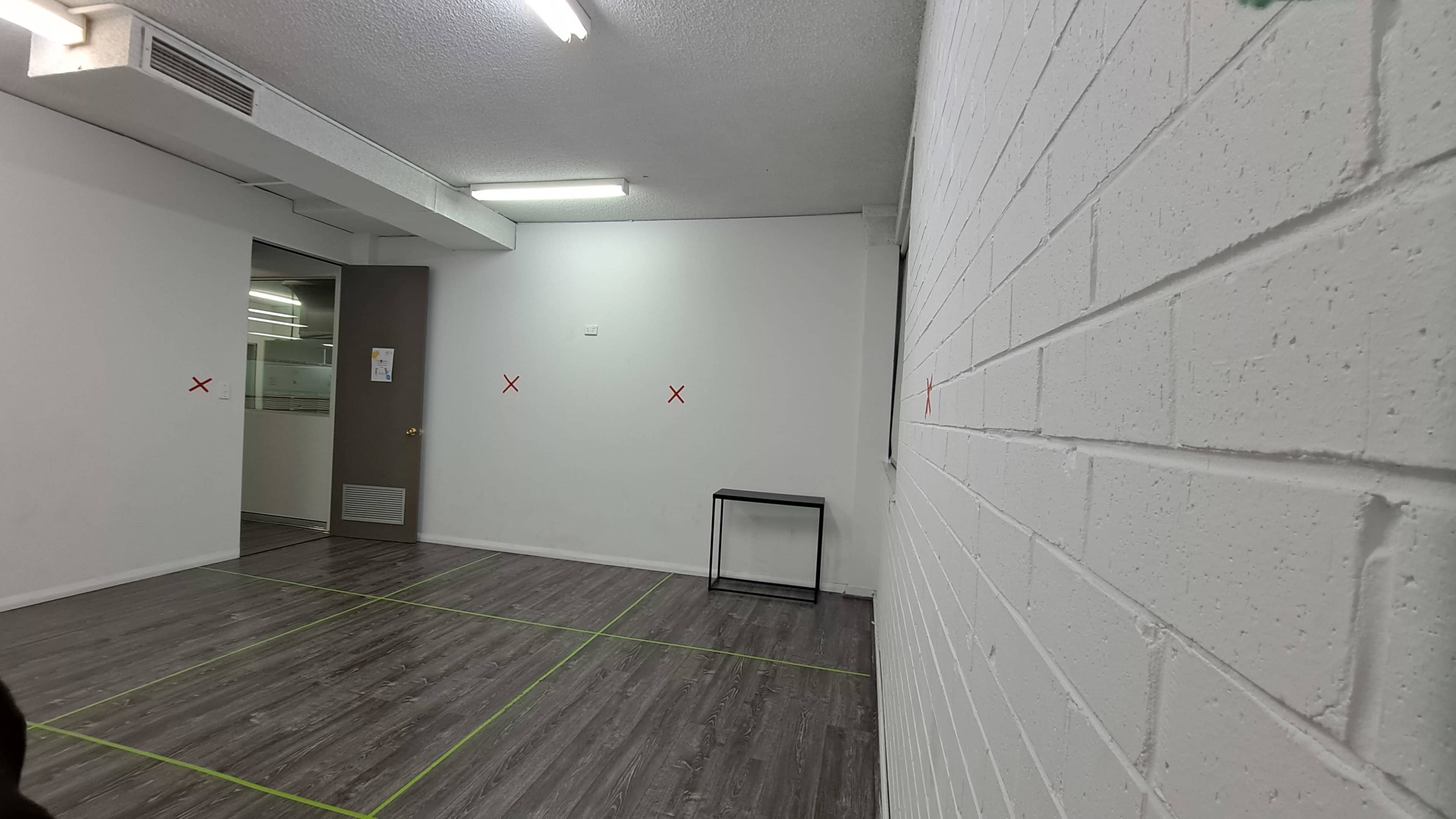 A vacant room with a white brick wall, a small black table, and red X marks on the walls and floor.
