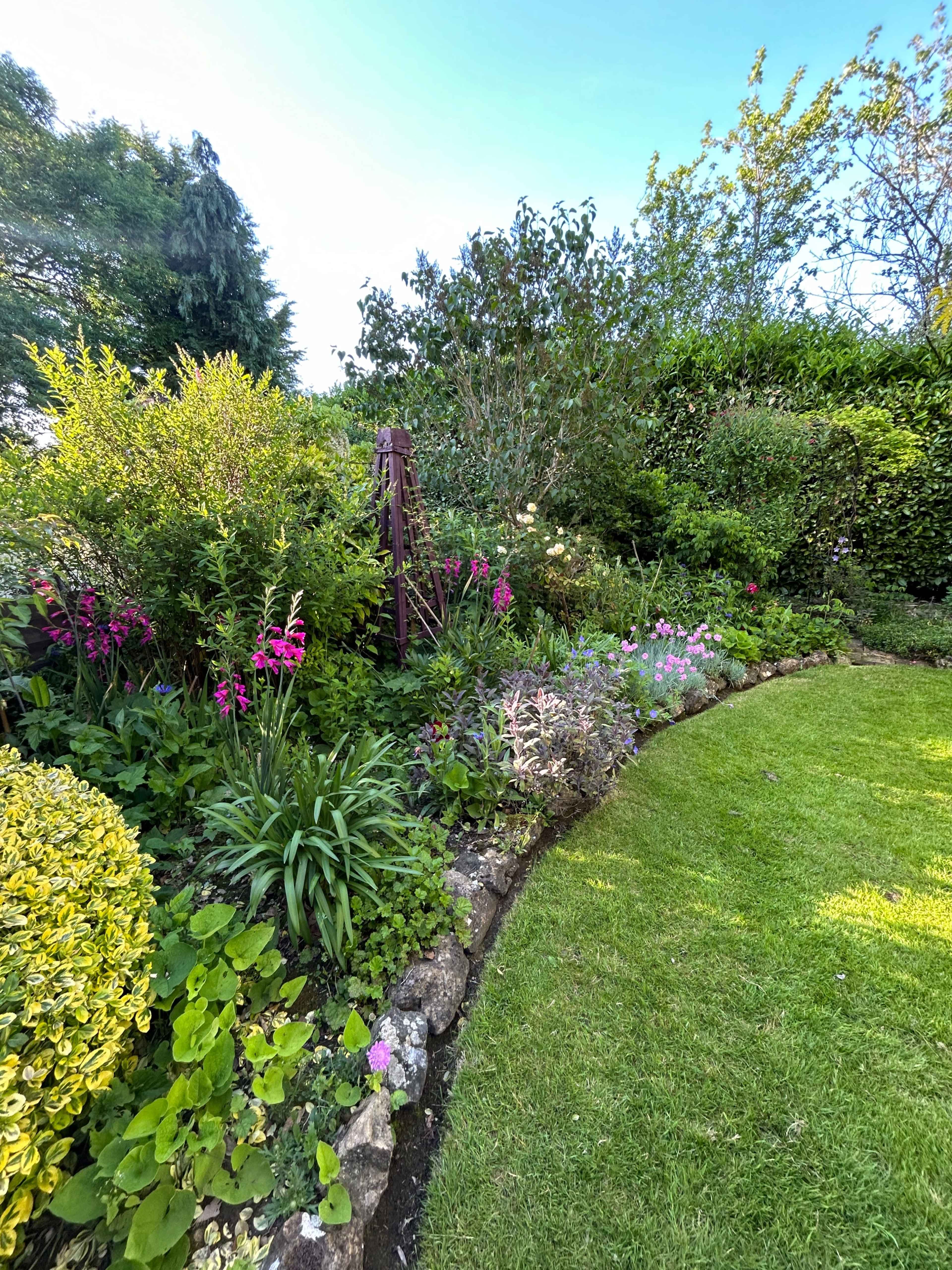 A well-maintained garden features a variety of colorful flowers and lush greenery along a curved stone border.