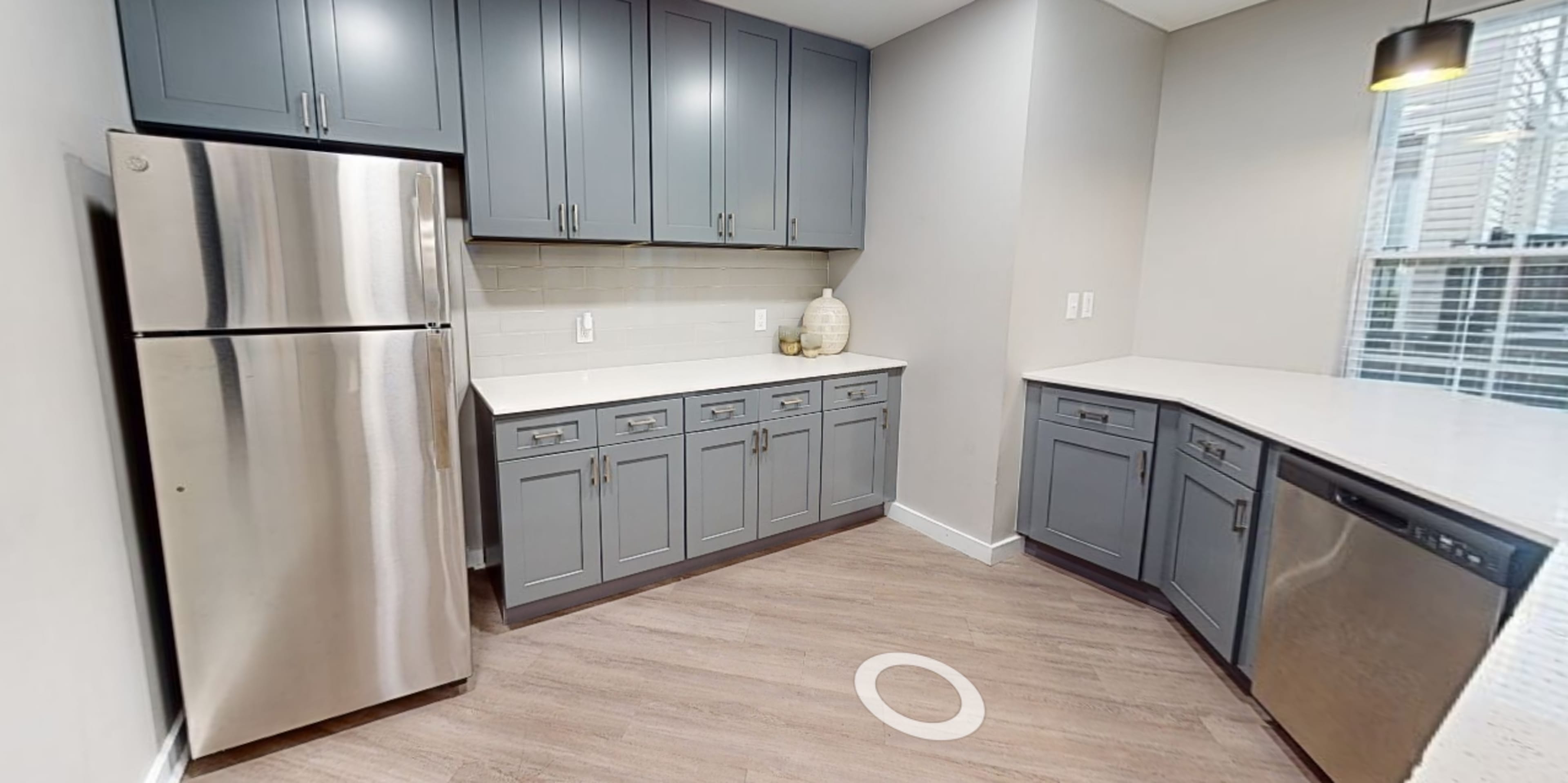 A modern kitchen featuring gray cabinets, stainless steel appliances, and white countertops with a light wood floor.