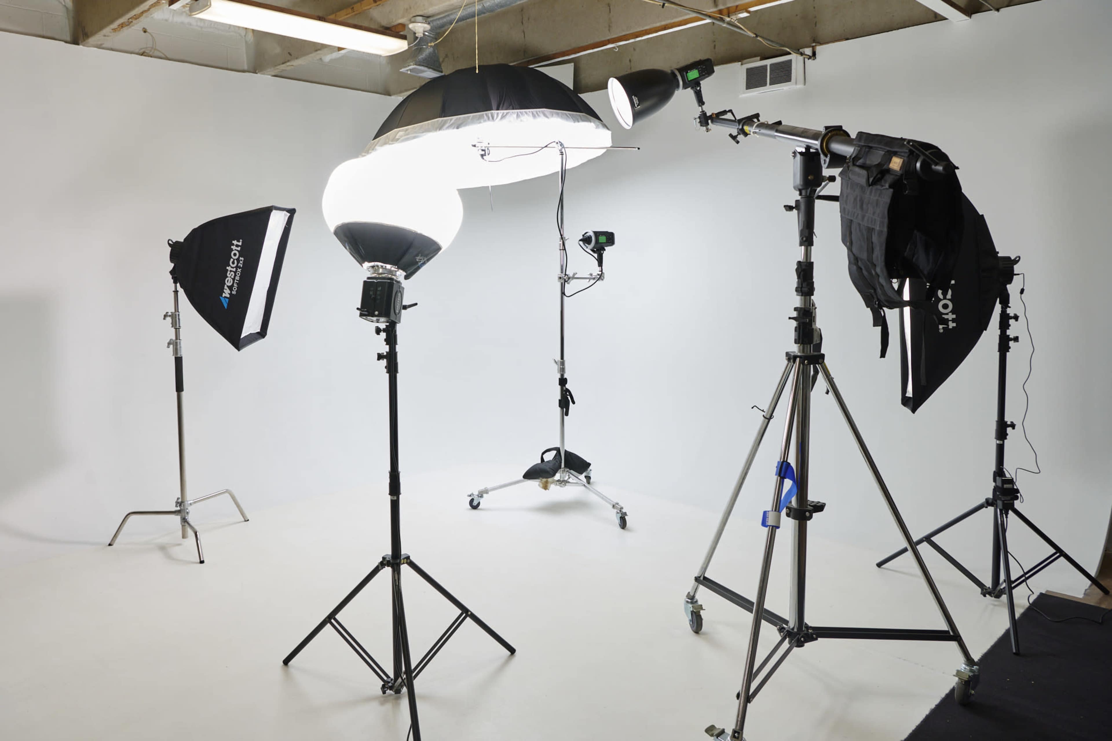 The image shows a photography studio setup with two softbox lights, a large overhead light, and a backdrop, all arranged on stands.