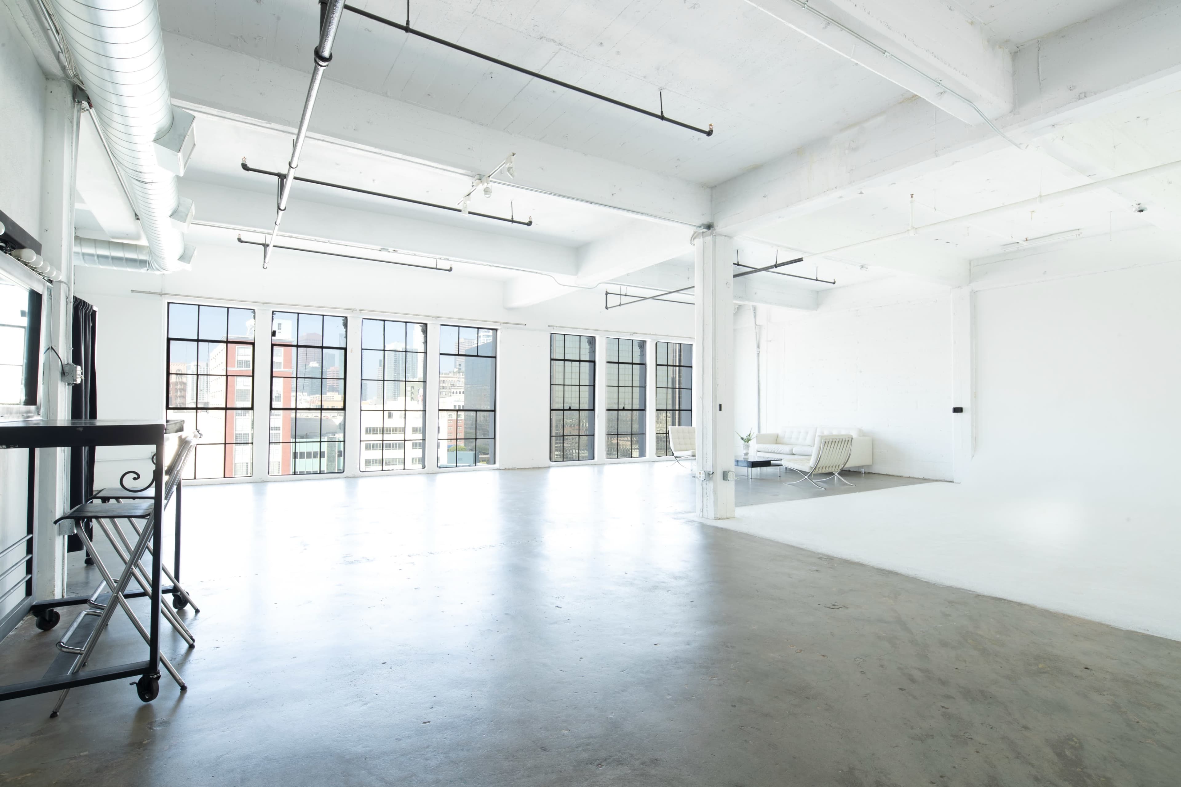 The image shows a spacious, bright studio with large windows and polished concrete flooring.