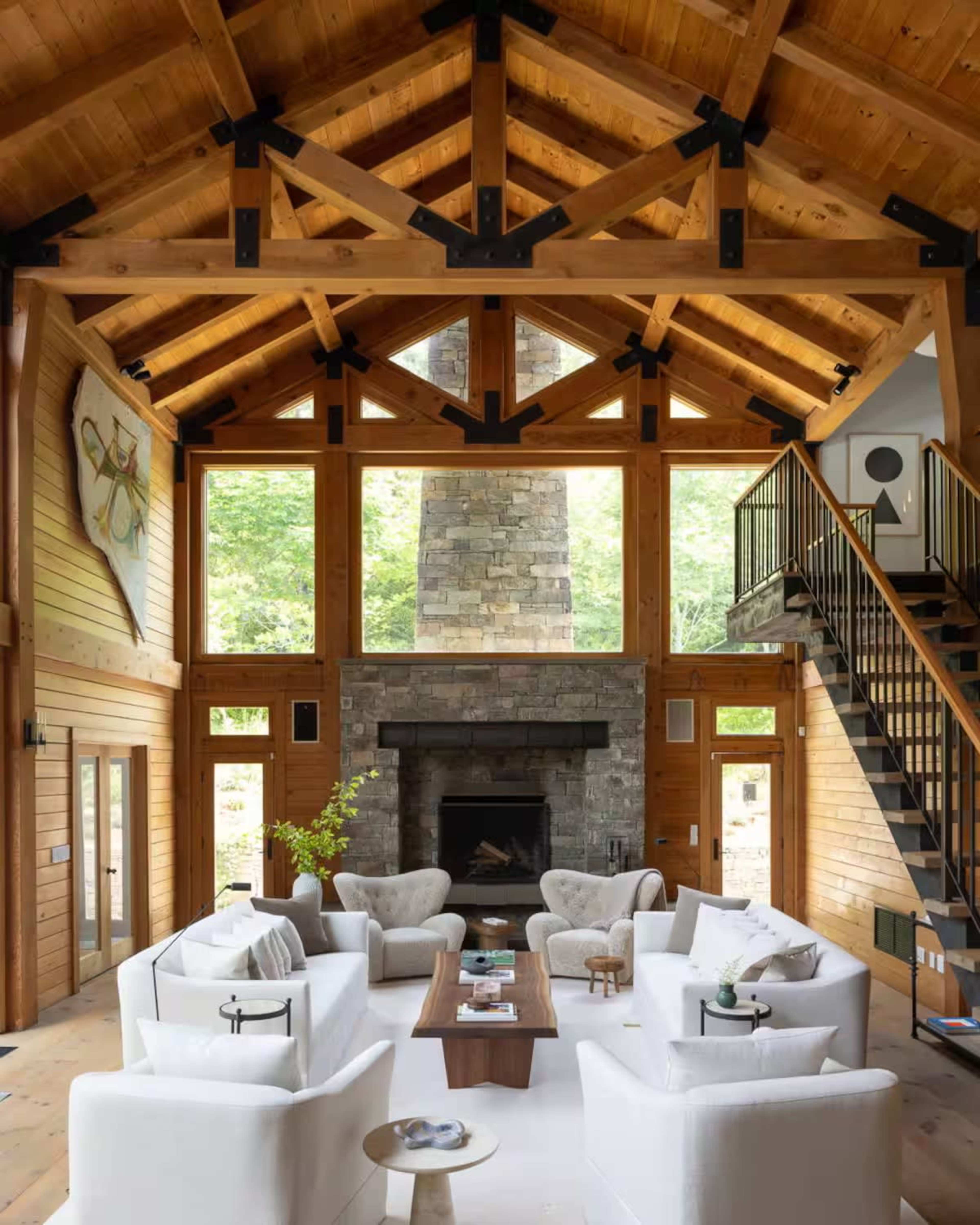 The image depicts a spacious living room with a high wooden-beam ceiling, a stone fireplace, and comfortable white sofas arranged around a coffee table.