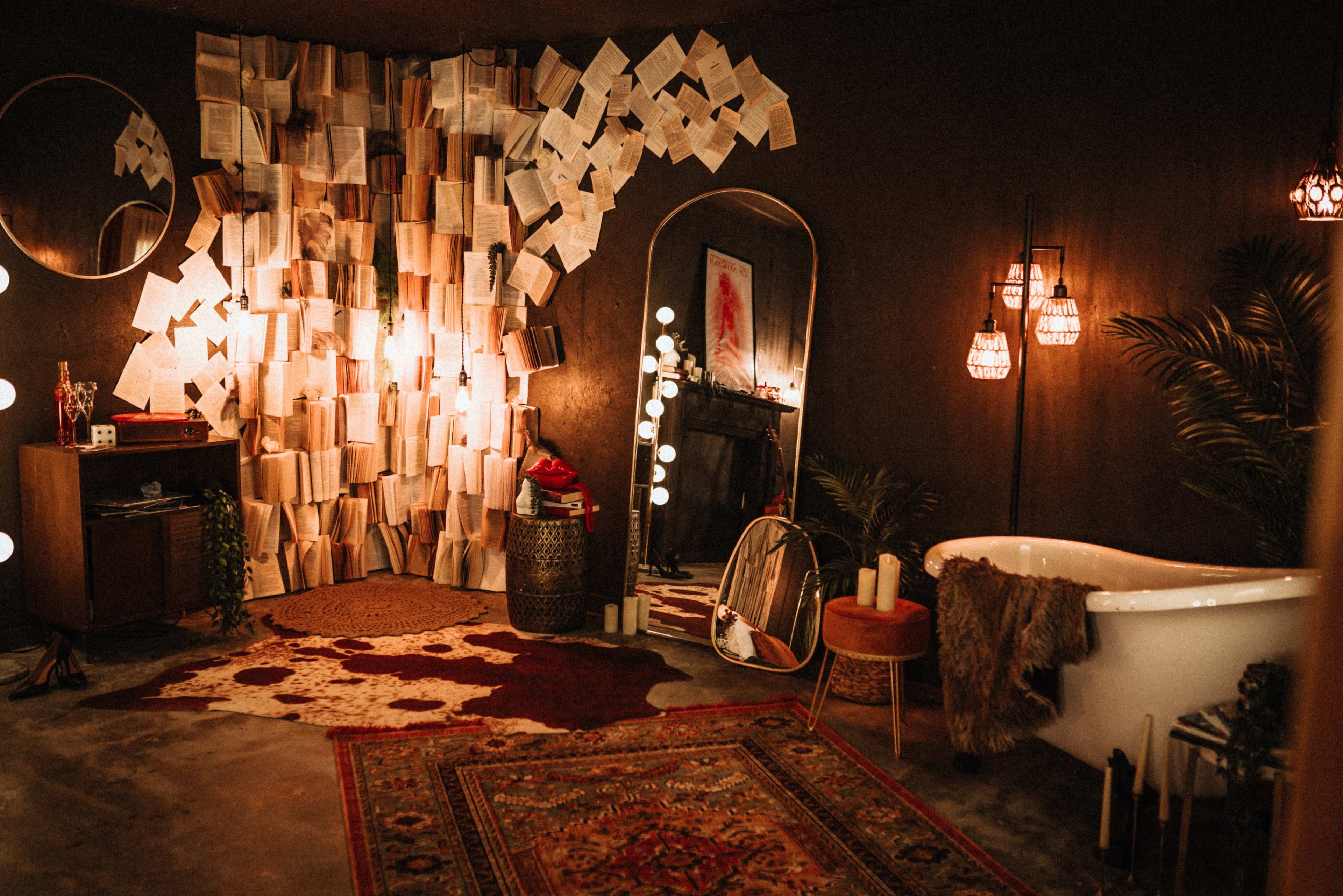 The image depicts a cozy room with a vintage bathtub, a wall adorned with scattered pages of books, and various decorative lighting elements.