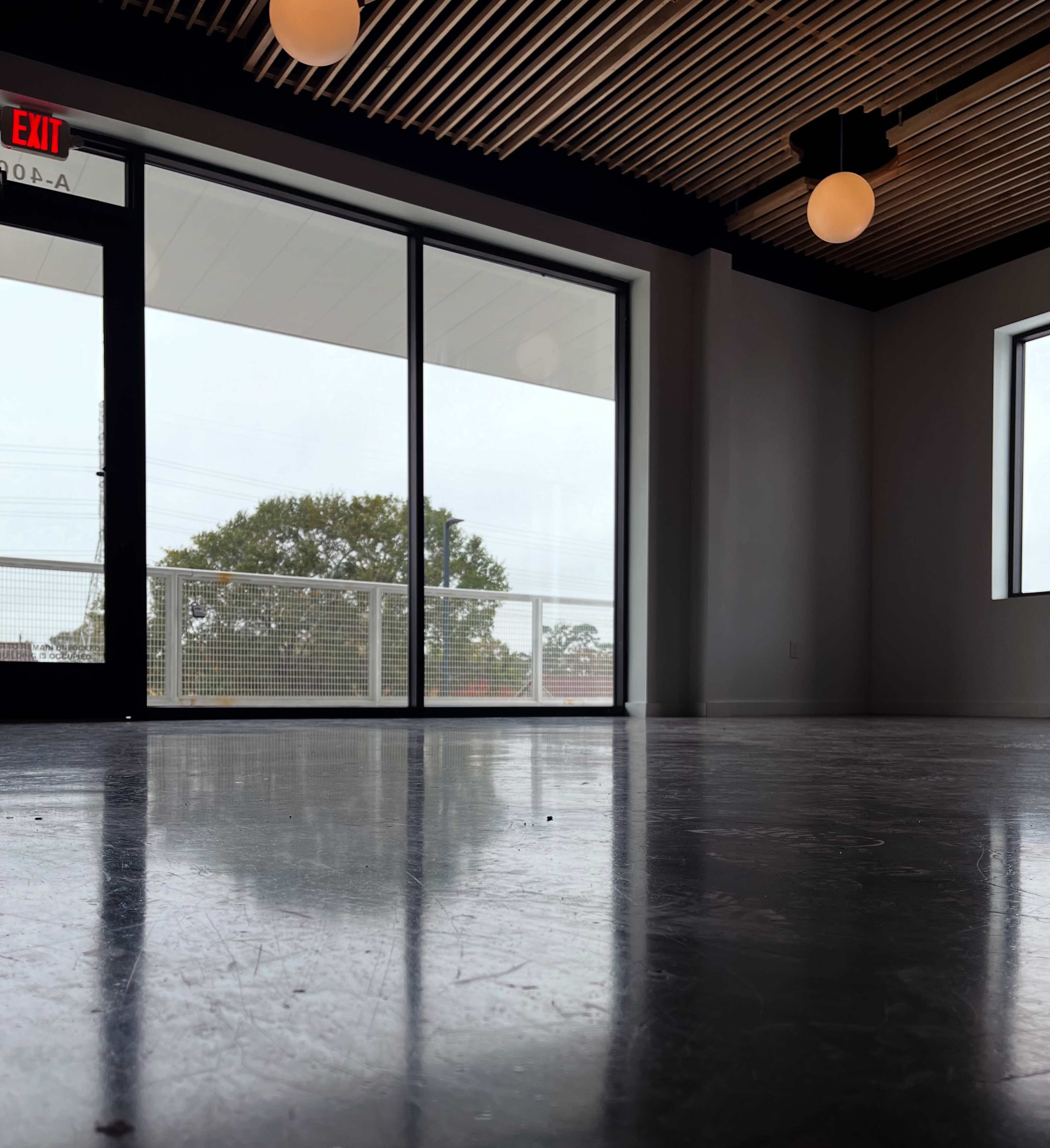 The image shows a spacious and minimalist interior with large windows overlooking an outdoor area and a smooth floor surface.